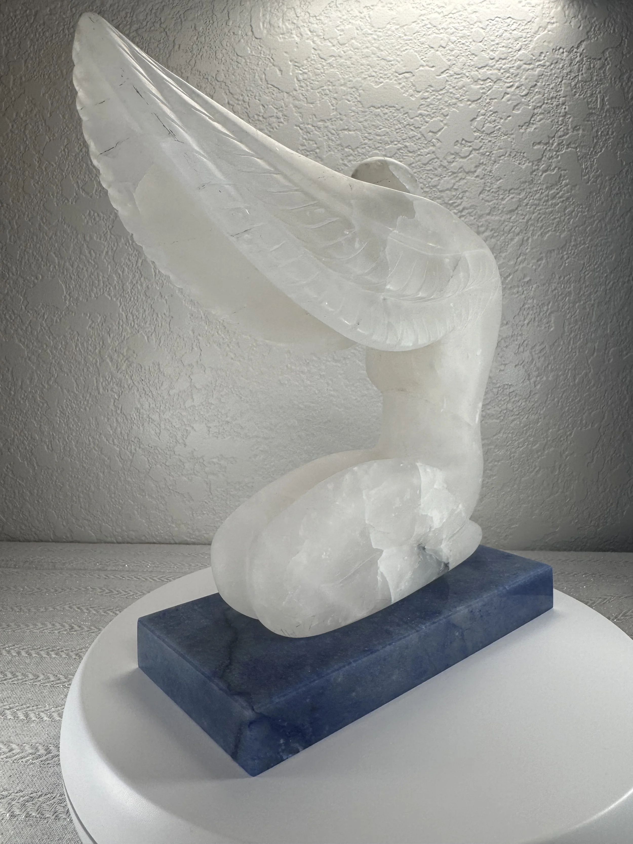 White marble sculpture of a bird, possibly an eagle or hawk, perched on a base, displayed on a white circular table.