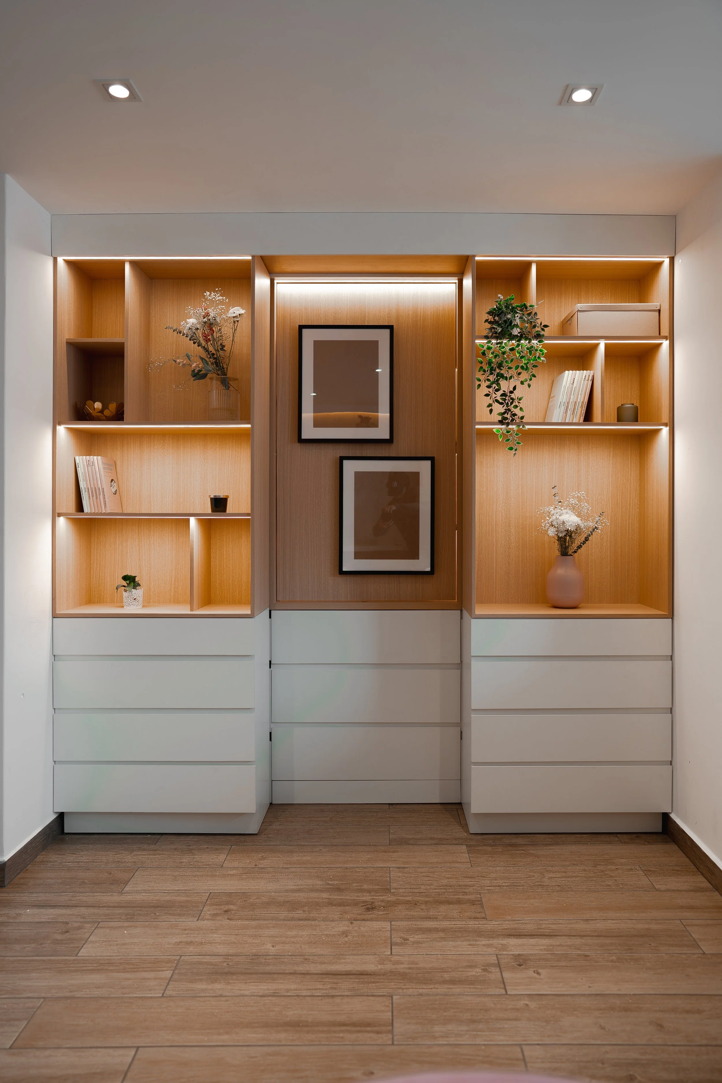 Estantería de madera con decoración, libros y plantas, con tres cuadros en la parte central