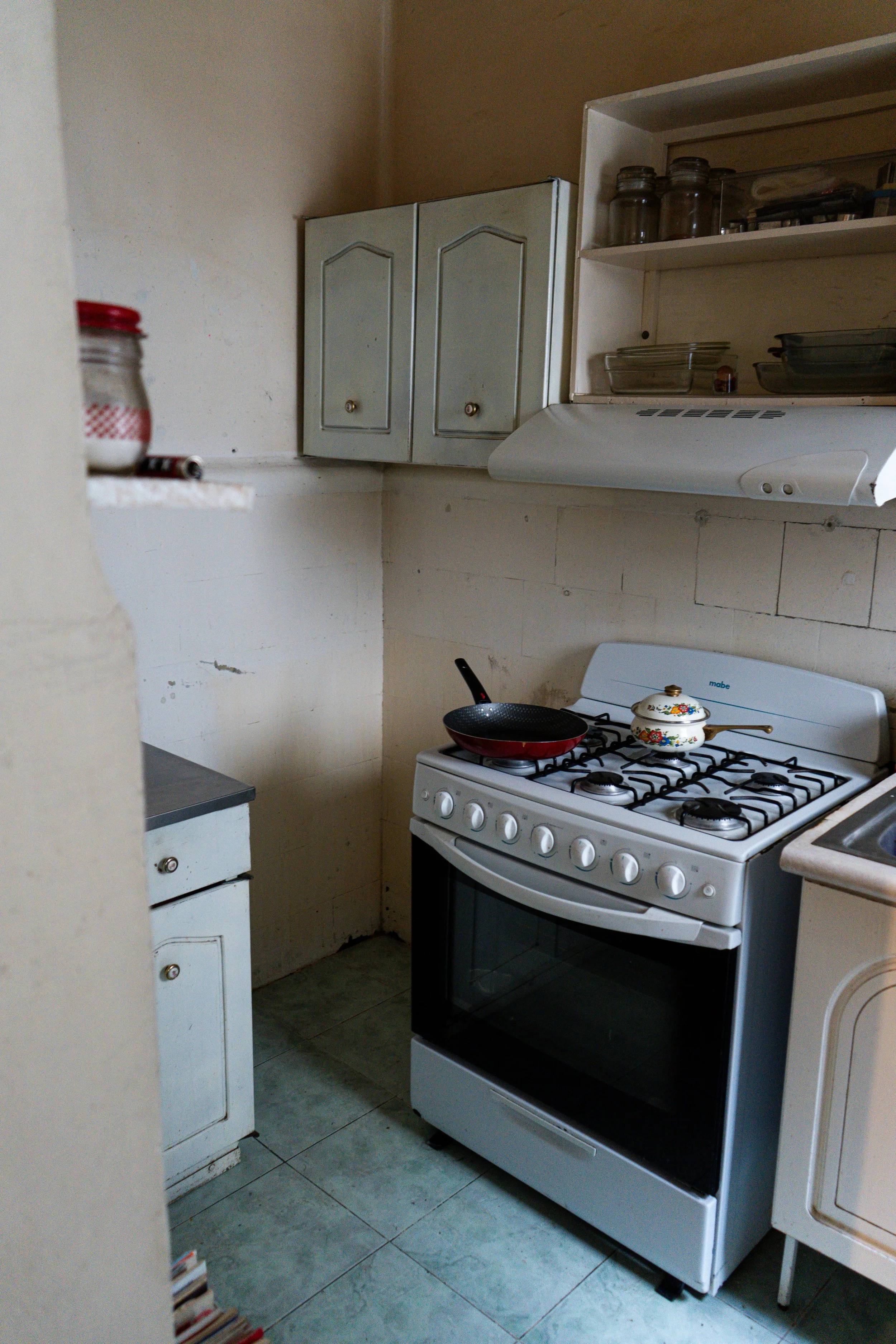 Cocina con estufa de cuatro quemadores, horno y horno microondas, estantería con frascos y platos, y balanza en la esquina.