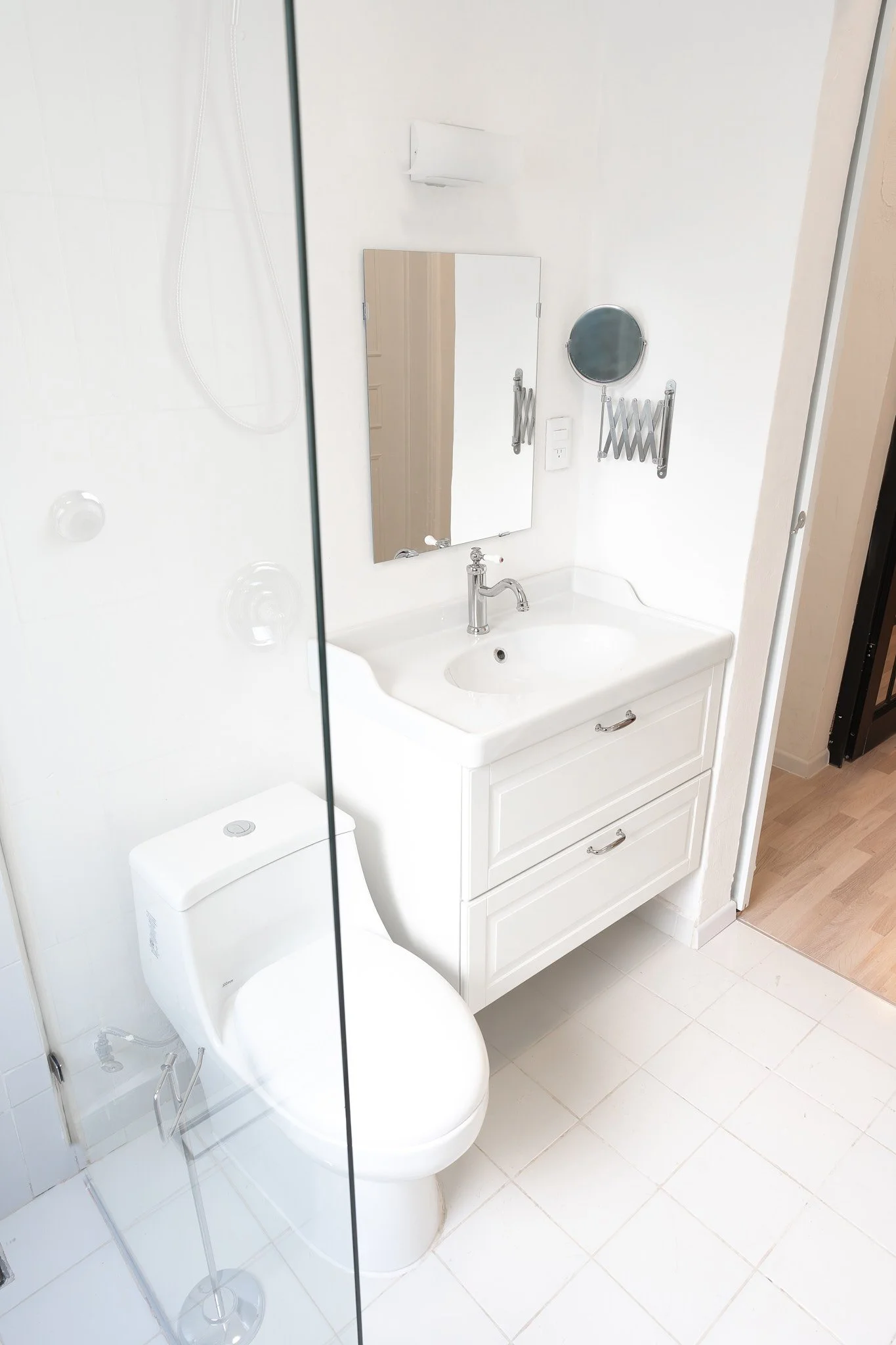 Baño con lavabo, espejo y cisterna, en un espacio pequeño, con paredes blancas y piso de baldosas blancas.