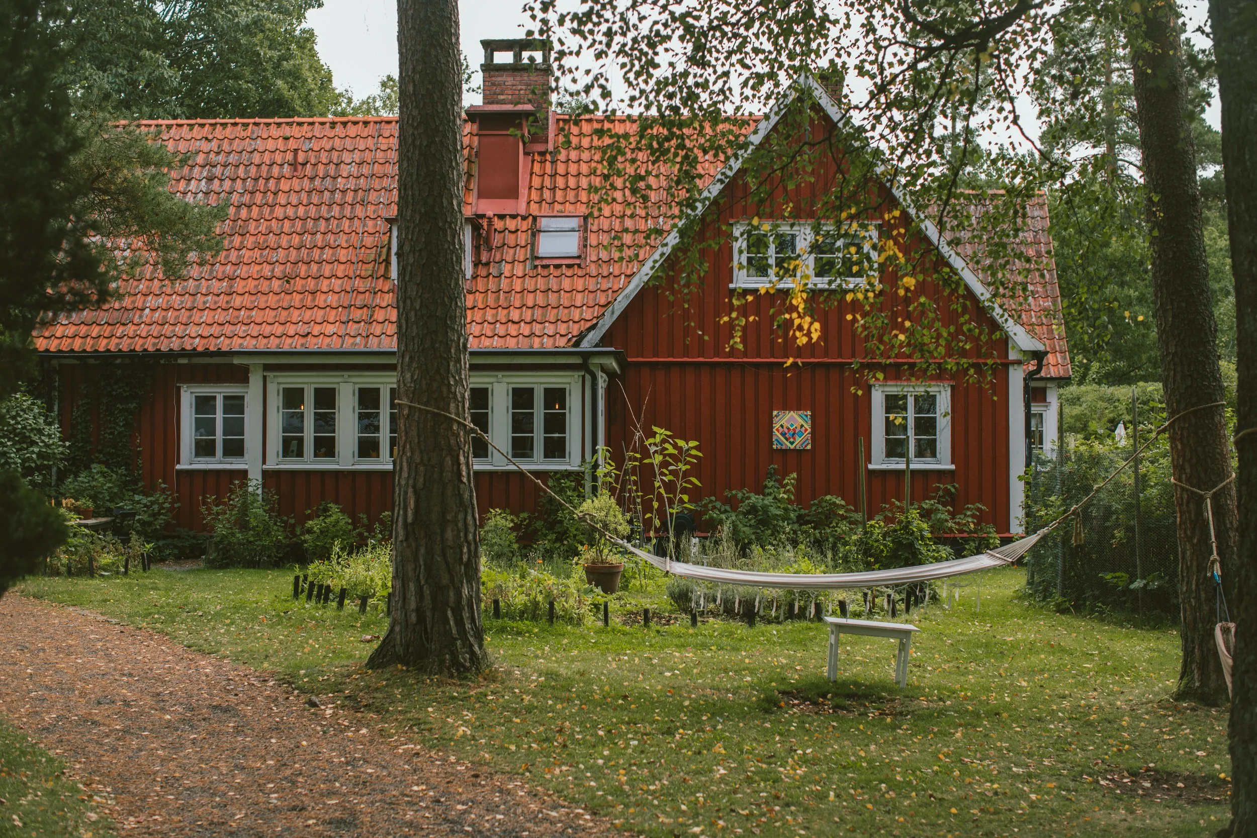 En röd trävilla med tegeltak omgivet av träd och en trädgård med utemöbler.