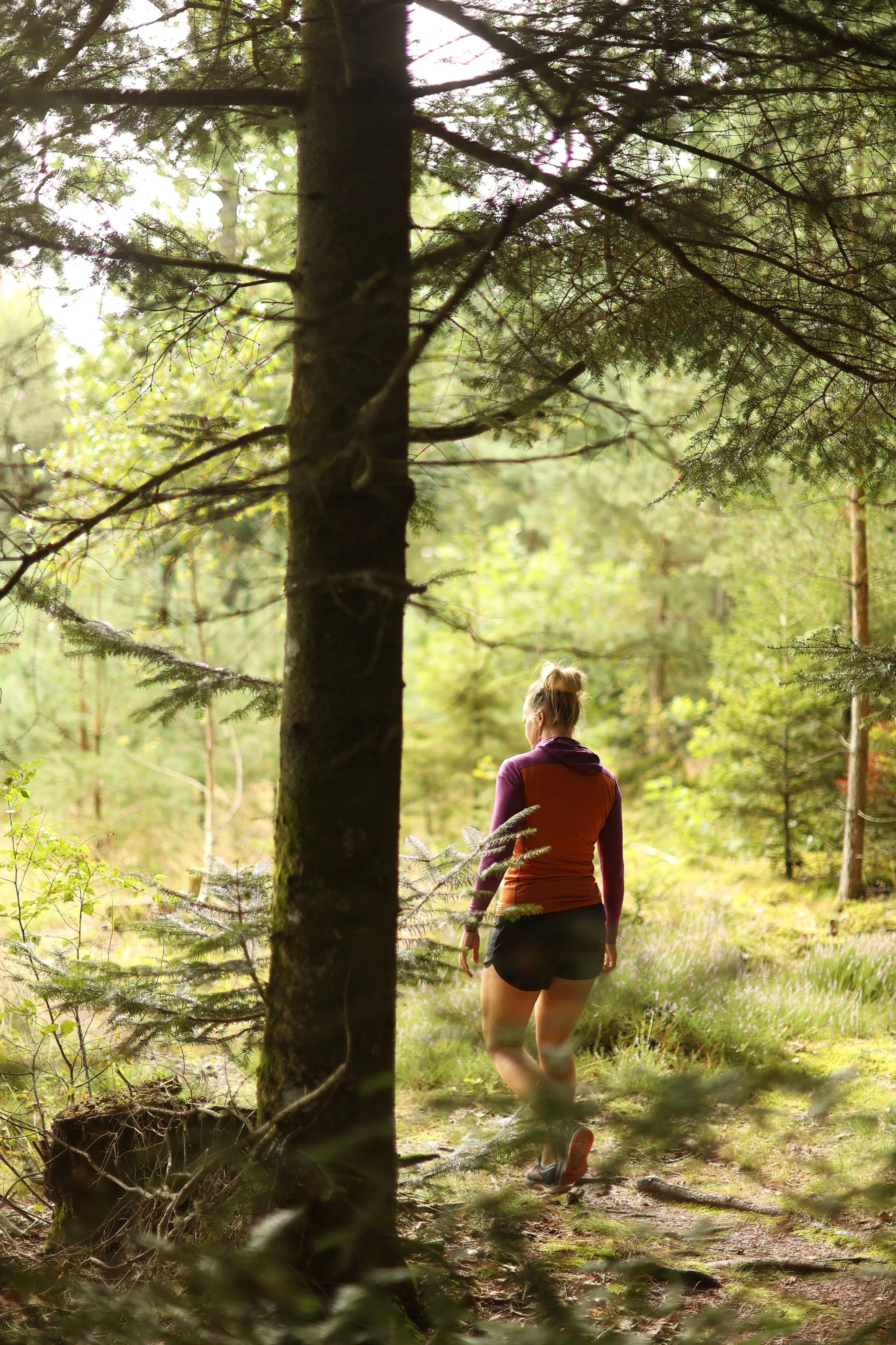 En kvinna joggar på en skogsstig omgiven av gröna träd och vegetation, bär sportkläder och sneakers.