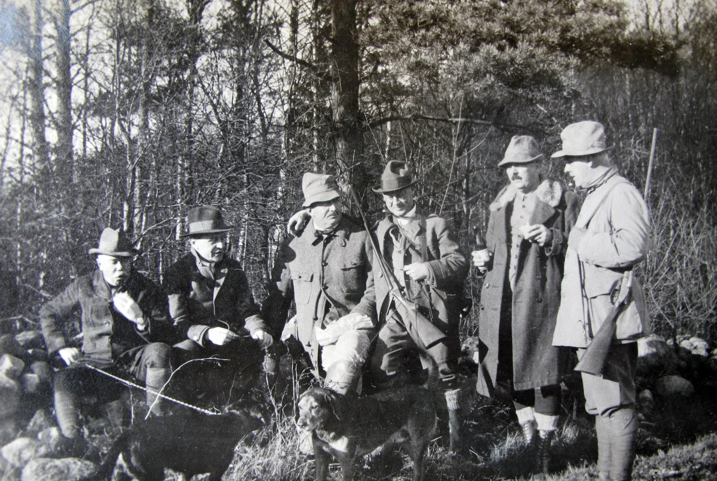 Grupp av jägare i äldre uniformer och hattar samlade i en skog.