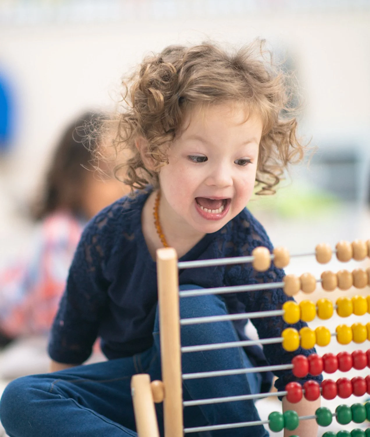 A young girl with curly hair and a blue shirt playing with an abacus.