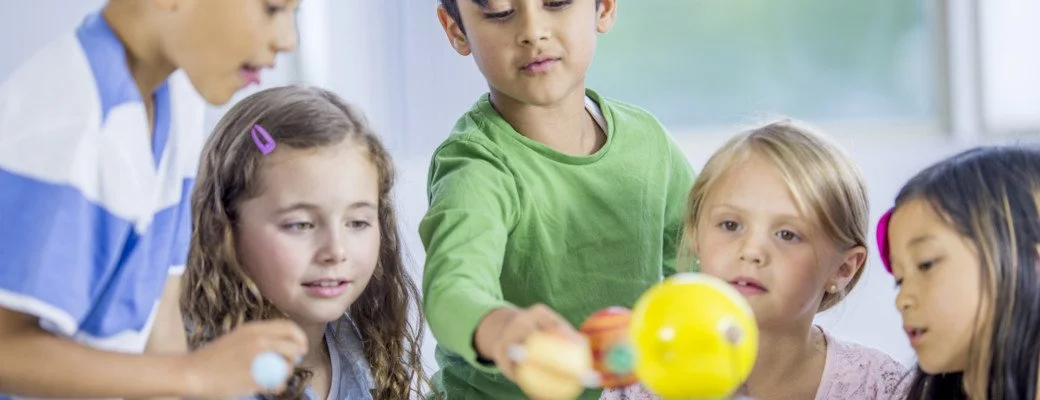 Group of children with a teacher examining a planetary model in a classroom.