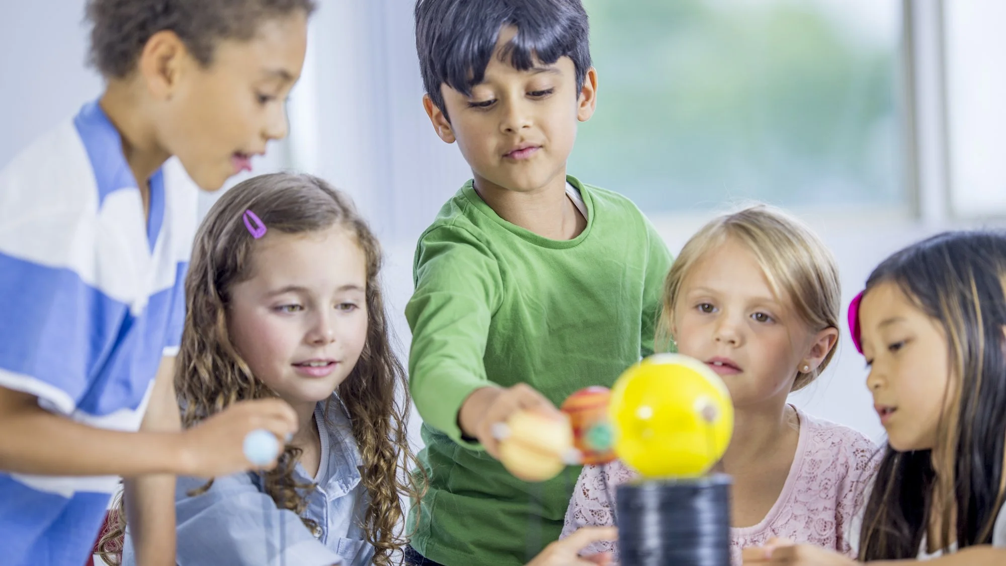 Children gathered around a table, playing with colorful plastic eggs inside a bright room.