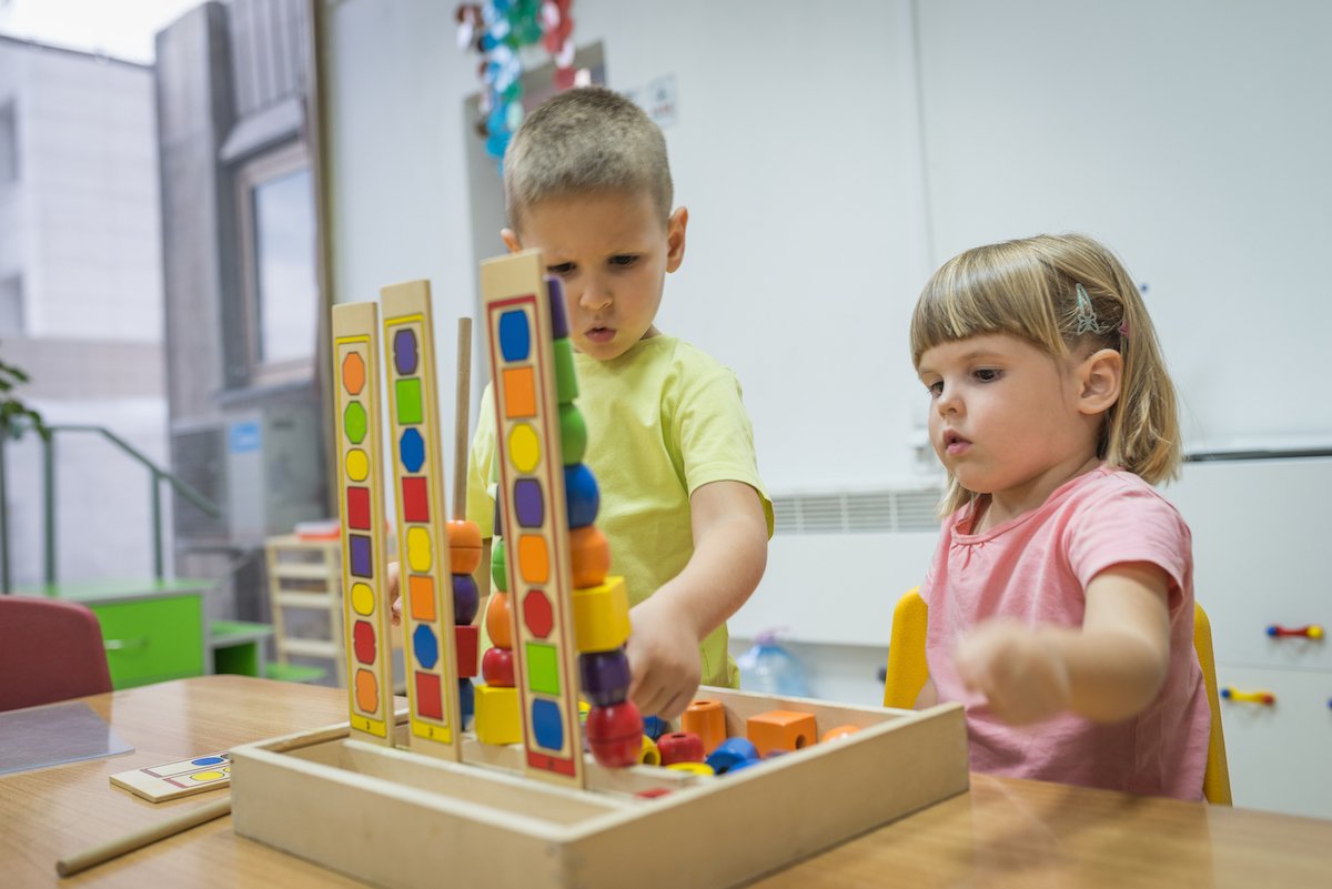 Two young children playing with colorful wooden stacking and sorting toys at a table in a classroom