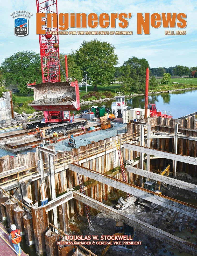 Construction workers operating machinery at a construction site near a body of water, with a large red crane lifting debris and heavy steel beams forming the structure of a building.