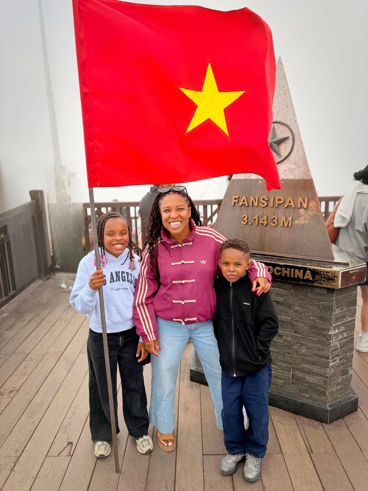 Un groupe de personnes souriantes avec le symbole de la pancarte de la cuisine chinoise et un drapeau jaune en rouge avec une étoile jaune dans la moitié supérieure, dans le contexte d'une visite à un monument ou site touristique.