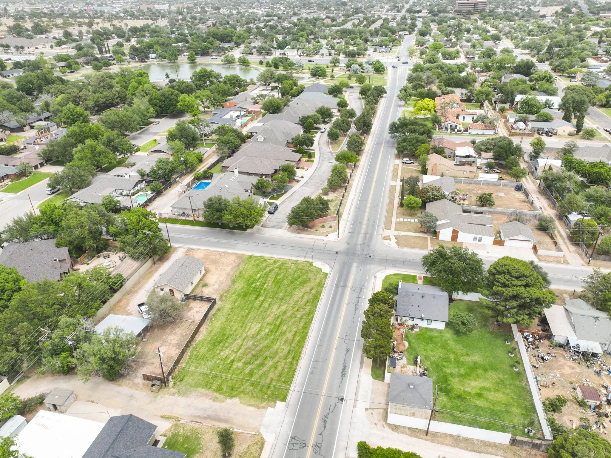 Aerial view of a suburban neighborhood with houses, trees, a pond, and a main road running through the area.