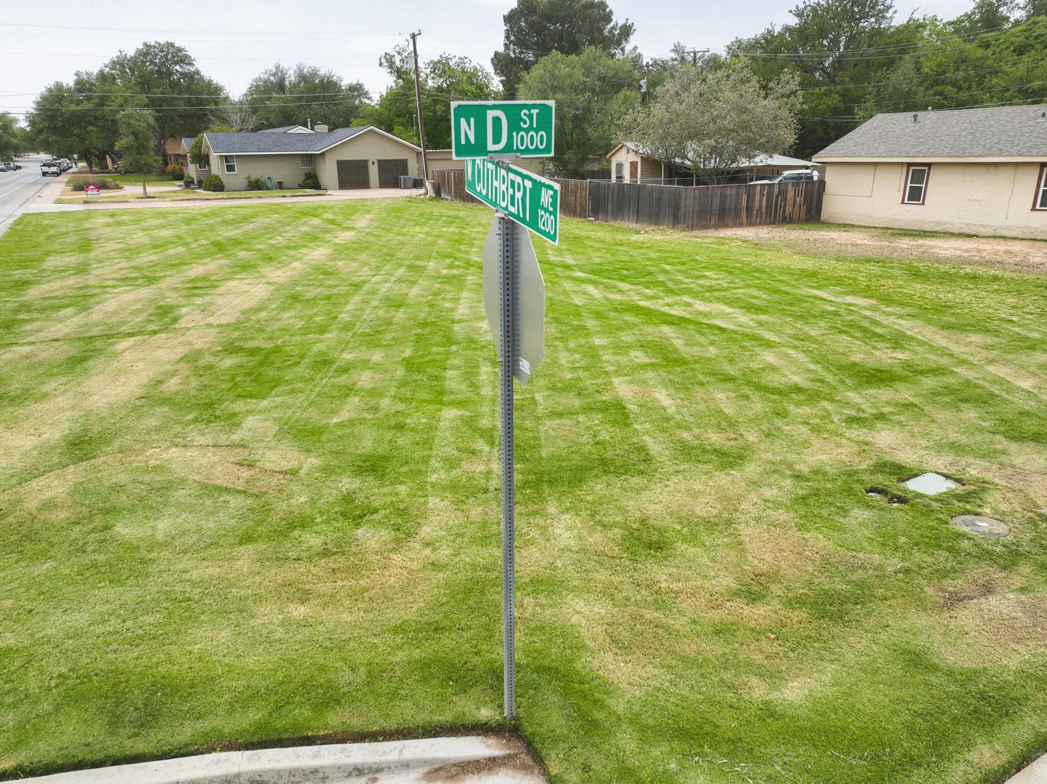 Street corner with green street signs indicating North D Street and South Tuthbert Avenue, residential houses, and a well-maintained grassy area.