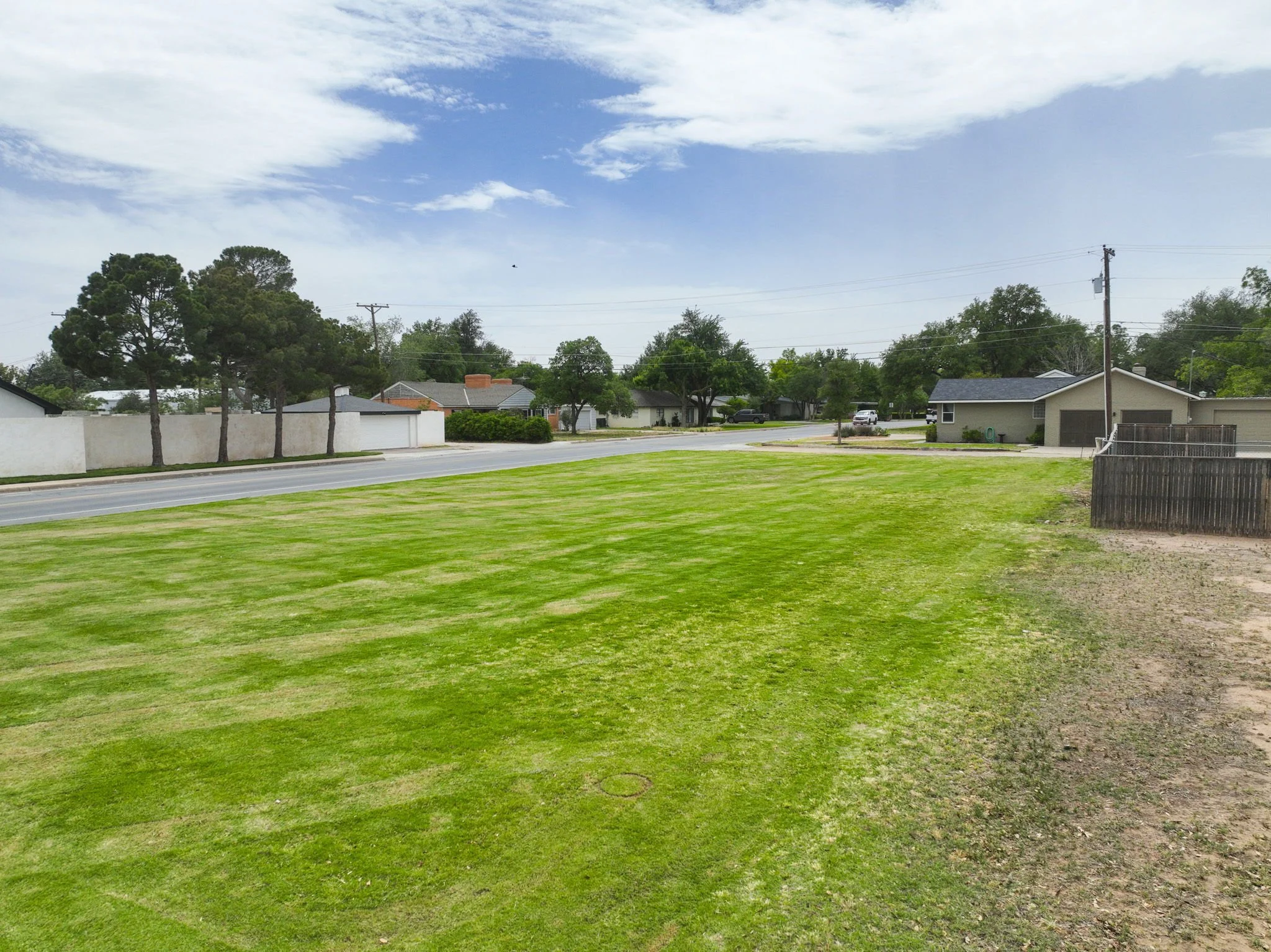 A suburban neighborhood with houses, trees, a street, and a grassy yard, under a partly cloudy sky.