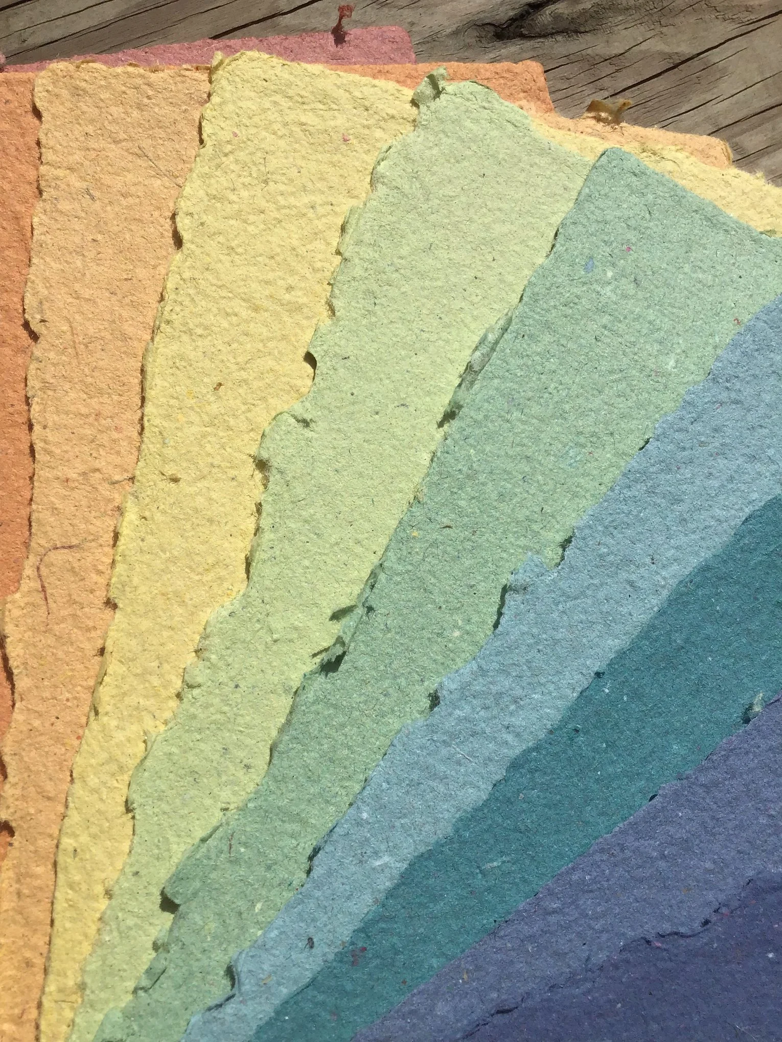 Colorful handmade recycled paper.  Colors shown are orange, light orange, yellow, spring green, green, light teal, dark teal, blue, and navy.