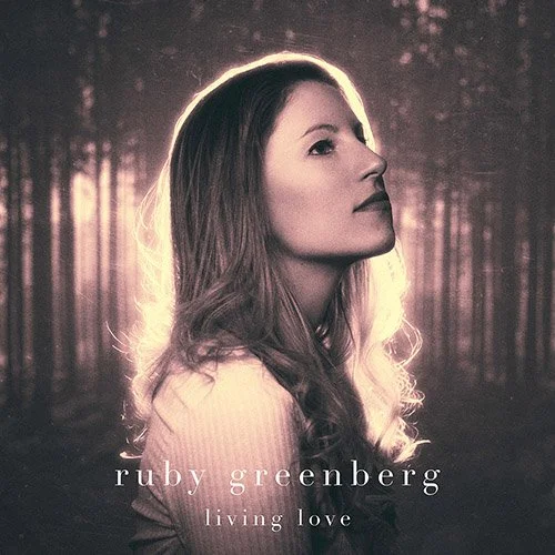 A woman with long wavy hair looking to the side, with a forest background and soft lighting. Album cover for Ruby Greenberg's "Living Love."