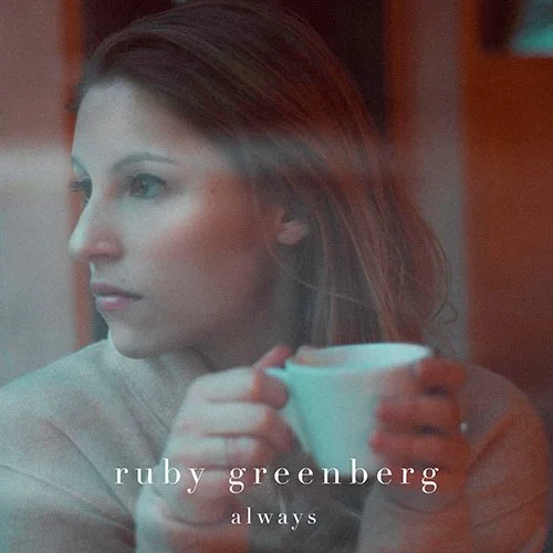 A woman with light skin and long brown hair holding a white mug, looking out a window with a pensive expression, with text overlay that says 'ruby greenberg always.'