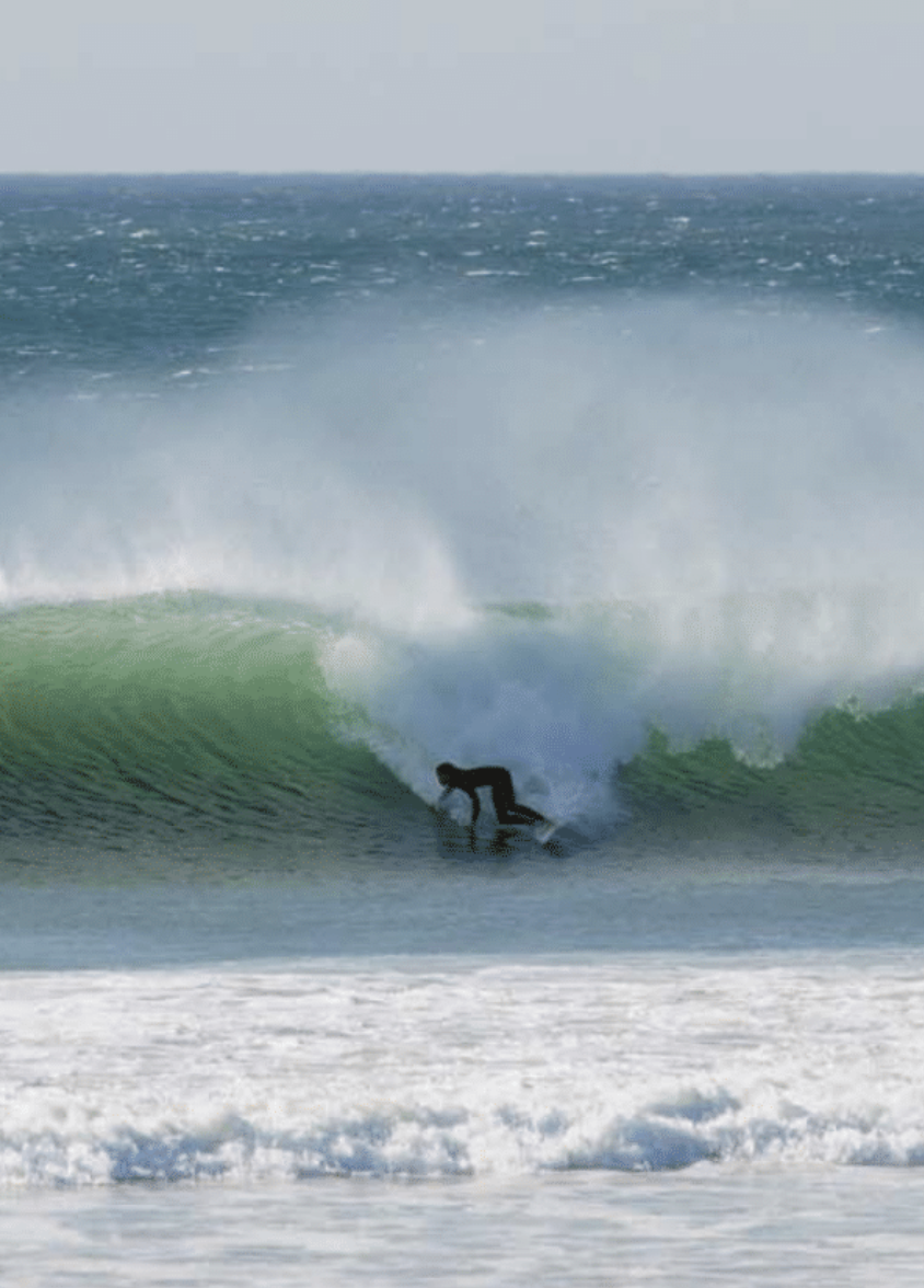 Ein Surfer fährt auf einer Welle im Meer, während die Welle bricht und Wasser spritzt.