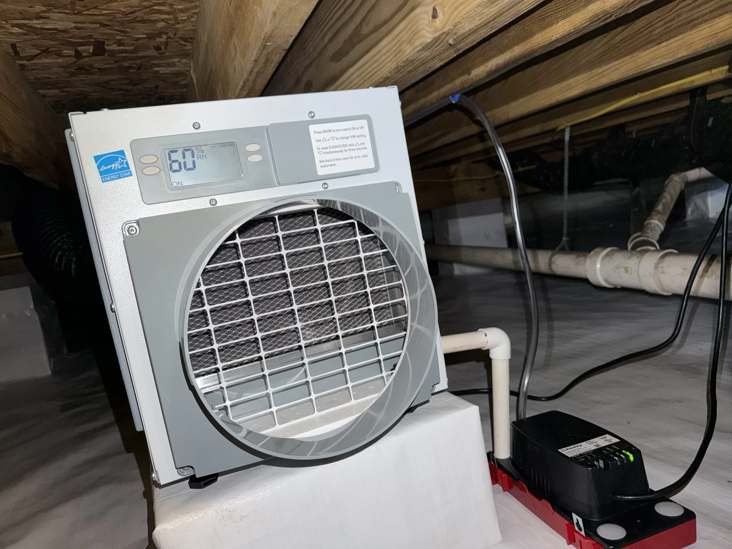 AprilAire crawl space dehumidifier with a condensate pump beneath mold-treated floor joists in a completed encapsulation designed to control humidity.