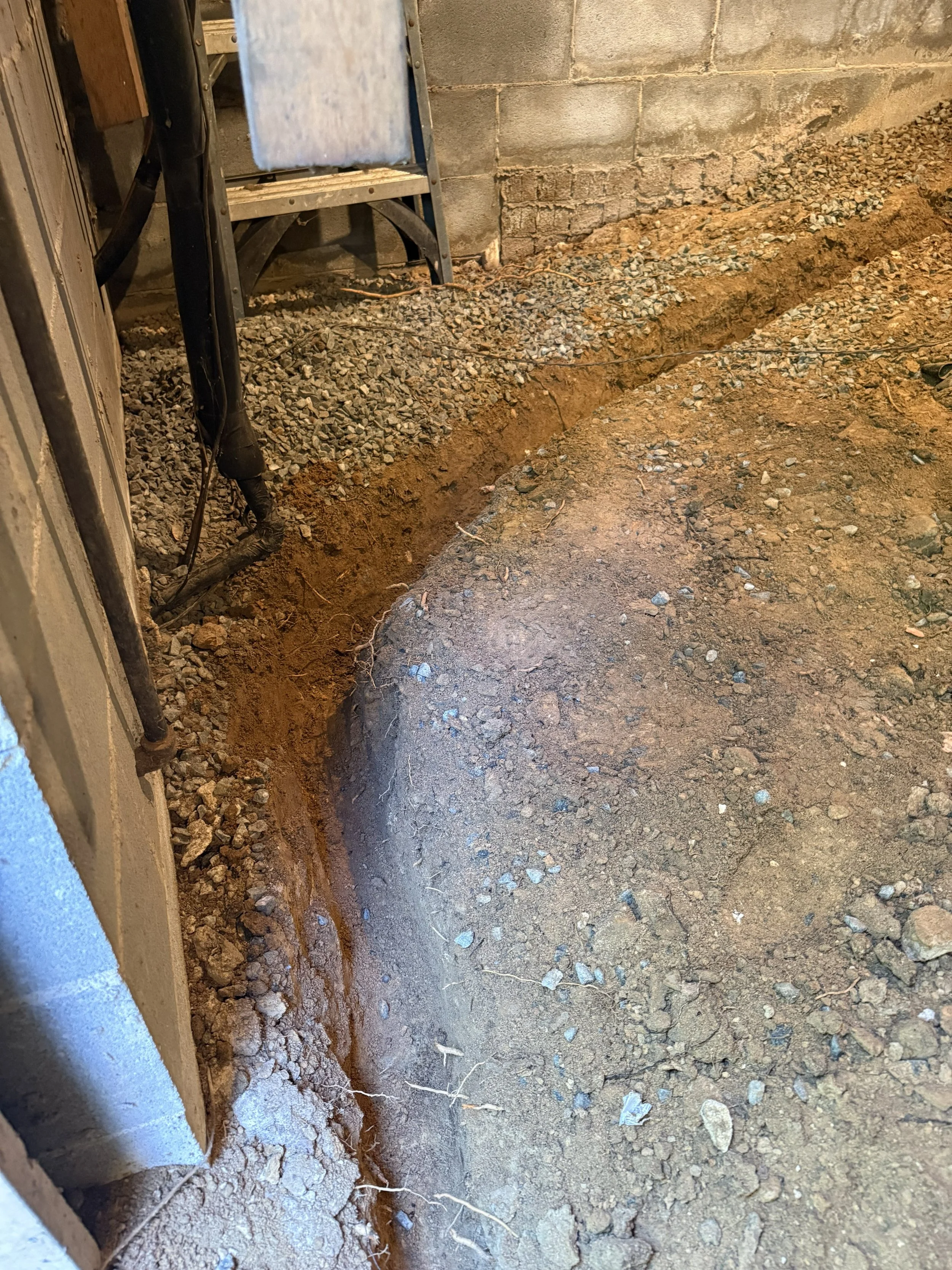 Interior crawl space drainage trench graded to direct water toward the sump pump.