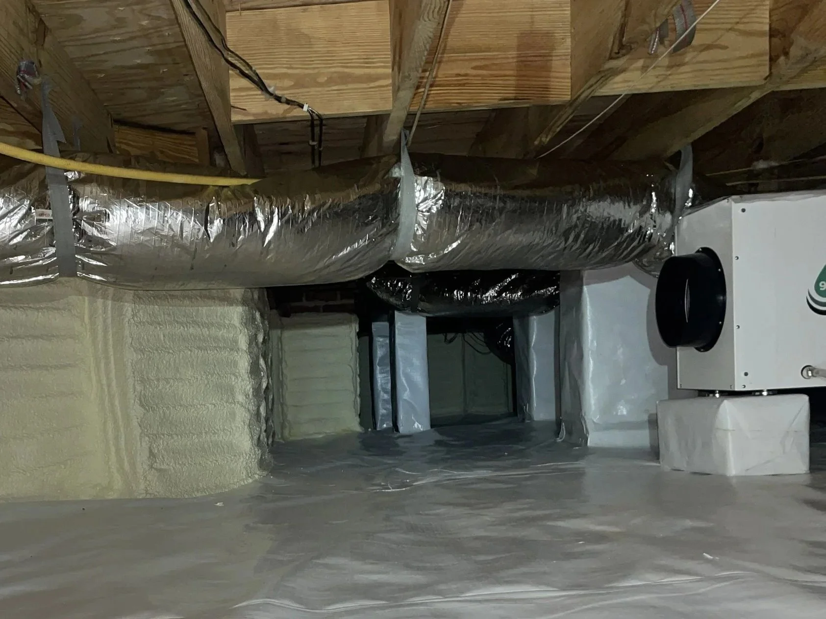 Encapsulated crawl space with sealed vapor barrier, spray foam foundation wall insulation, ductwork, and dehumidifier for moisture control.