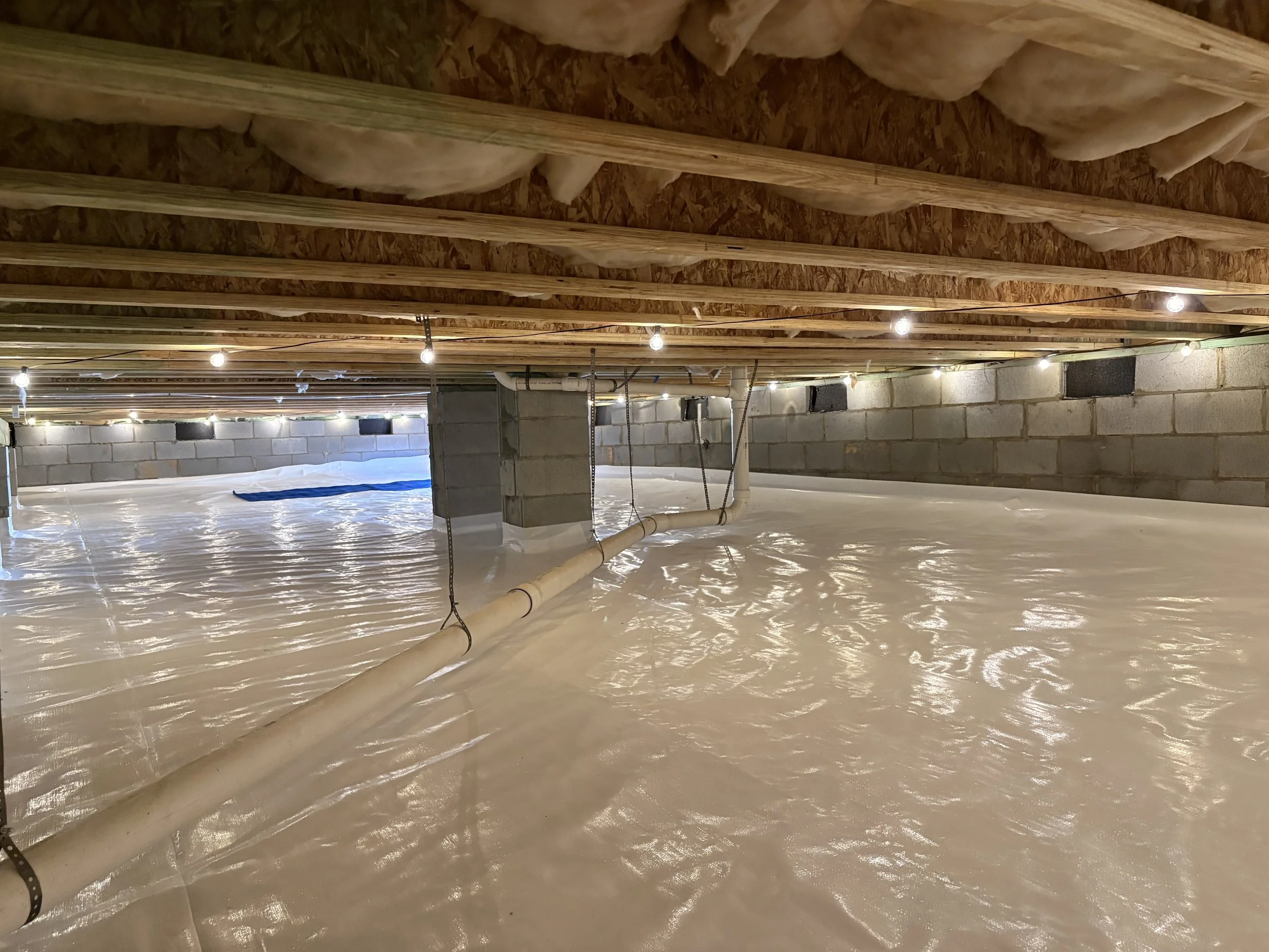 Ground vapor barrier installed across a crawl space floor with sealed seams and exposed foundation walls