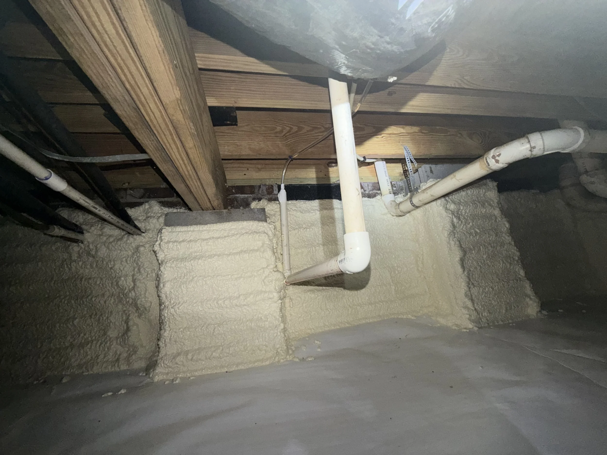 Close-up of mold-remediated crawl space joists above spray-foam insulation installed along the foundation walls.