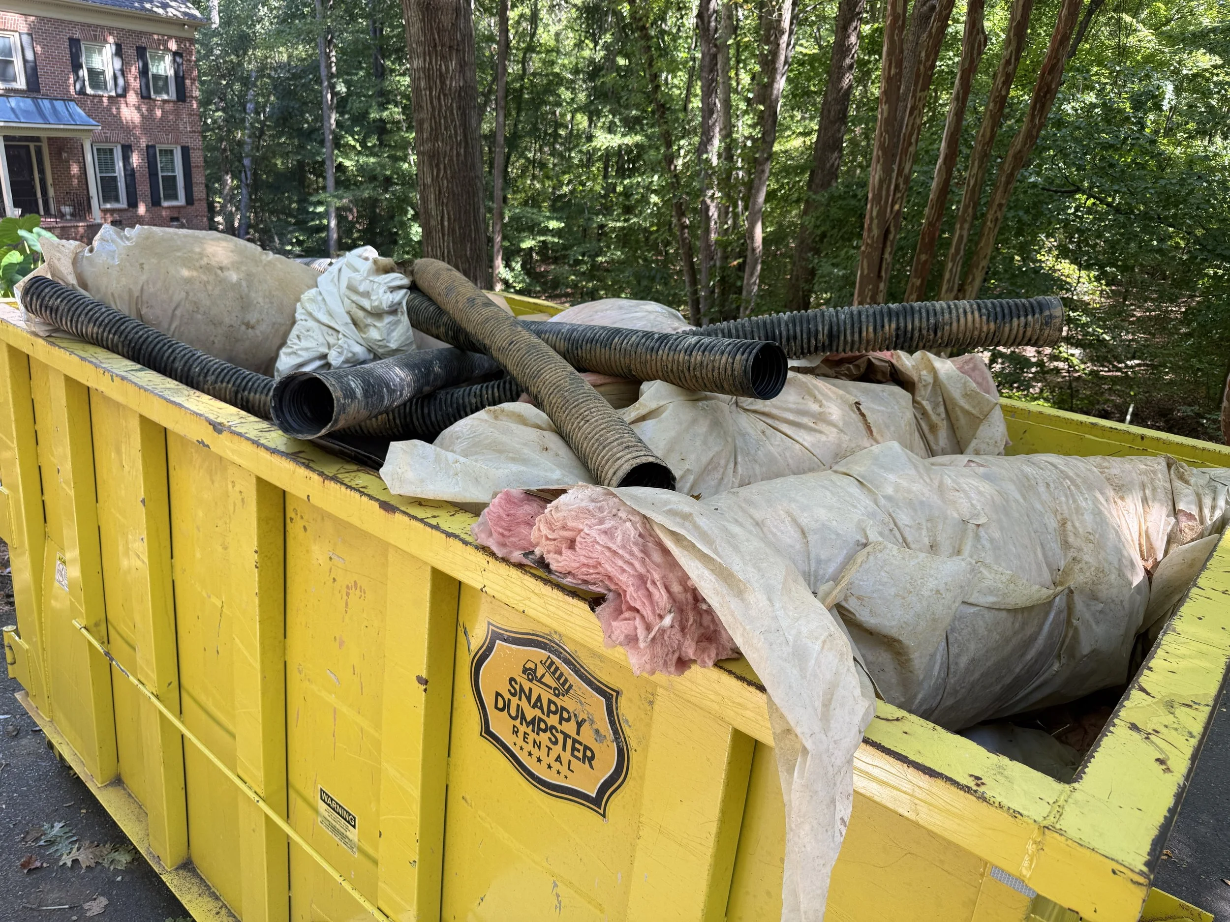 Dumpster filled with moldy insulation, an old vapor barrier, drainage pipe and debris removed during a crawl space cleanout.