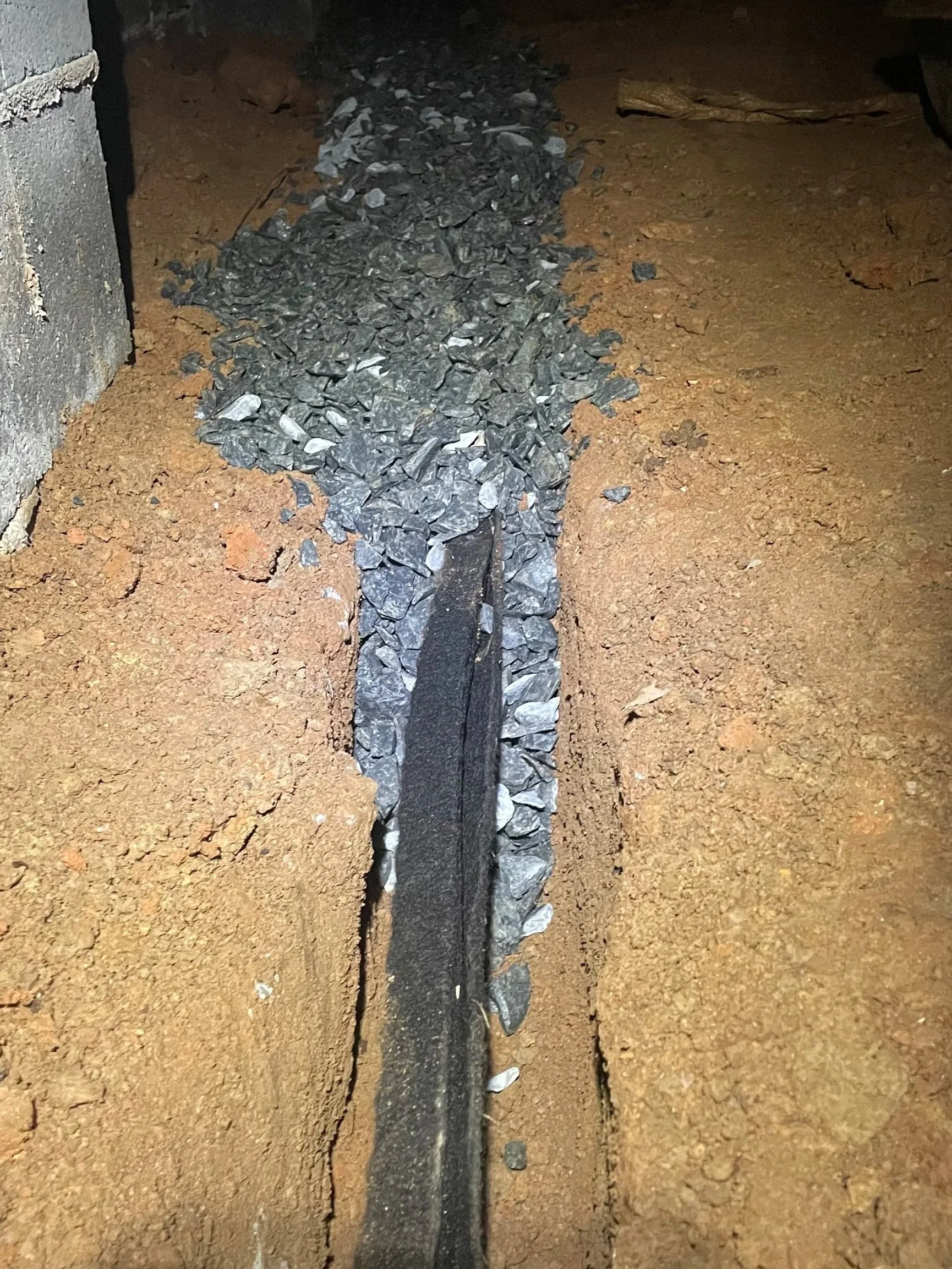 Crawl space drainage trench with drain channel installed and backfilled with gravel