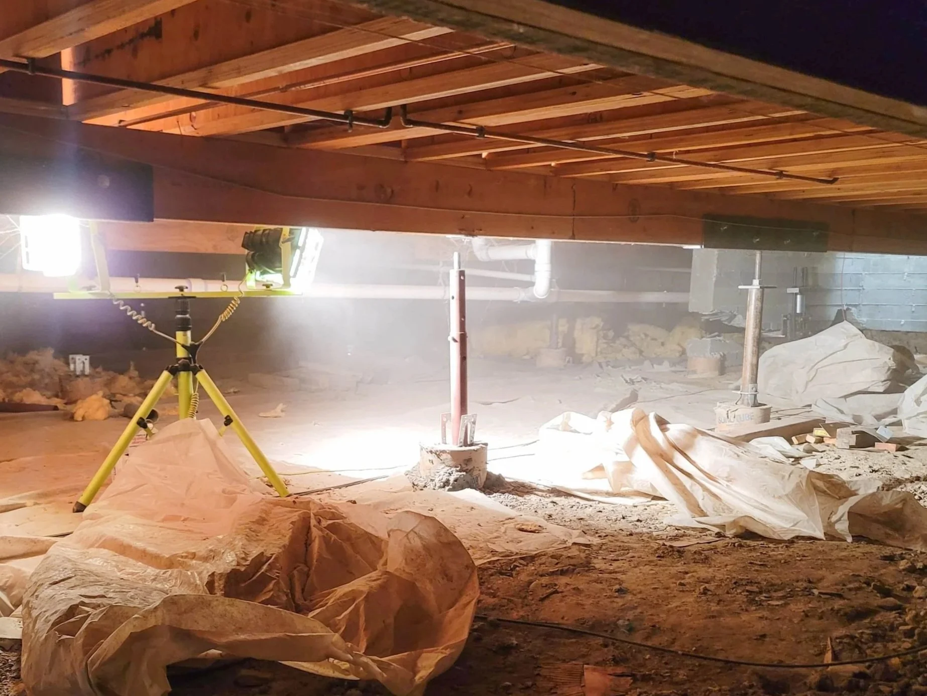 Crawl space structural wood repair with temporary support posts, repaired floor framing, exposed beams, and cleanout work under the home.