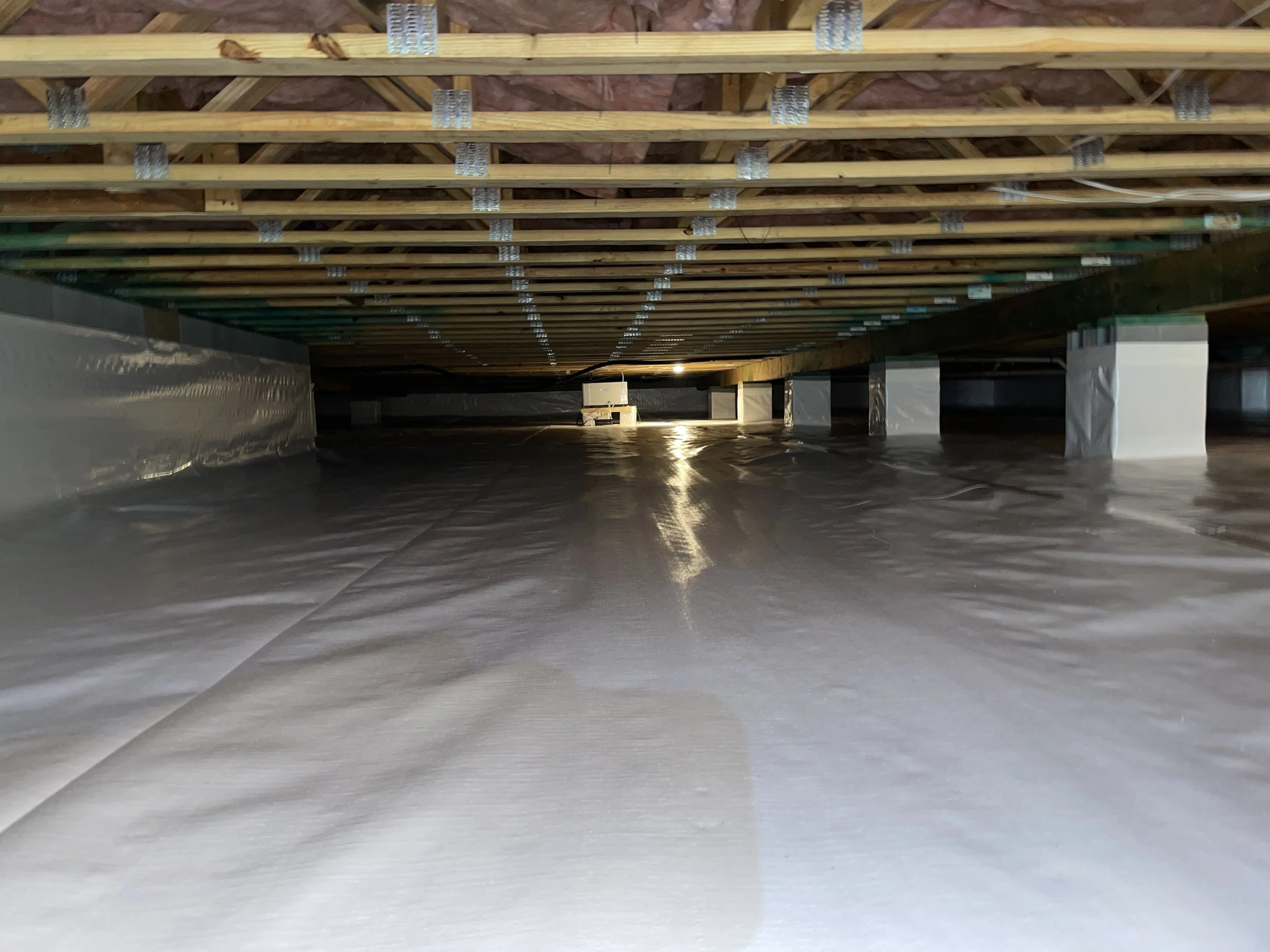 Crawl space with a sealed ground vapor barrier installed across the floor, walls and piers.
