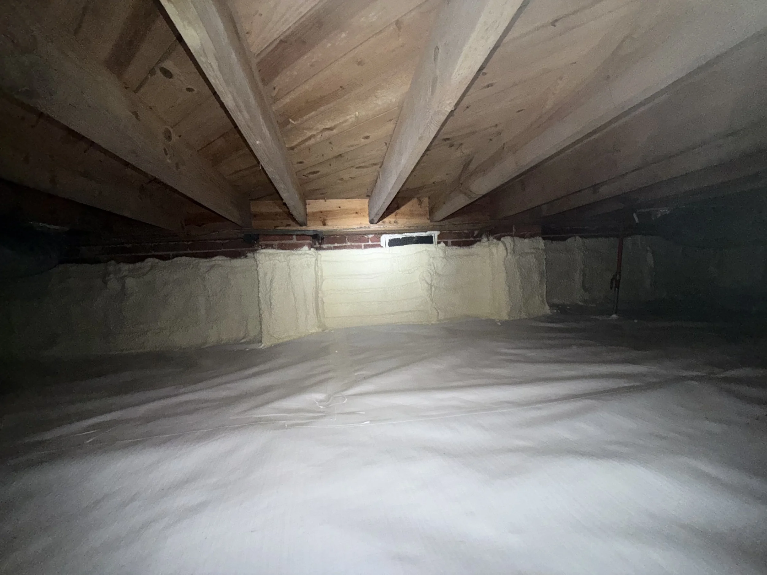 Completed crawl space encapsulation in a Charlotte-area home with sealed vents, a reinforced 20-mil liner, spray-foam foundation walls and clean floor joists after mold remediation.