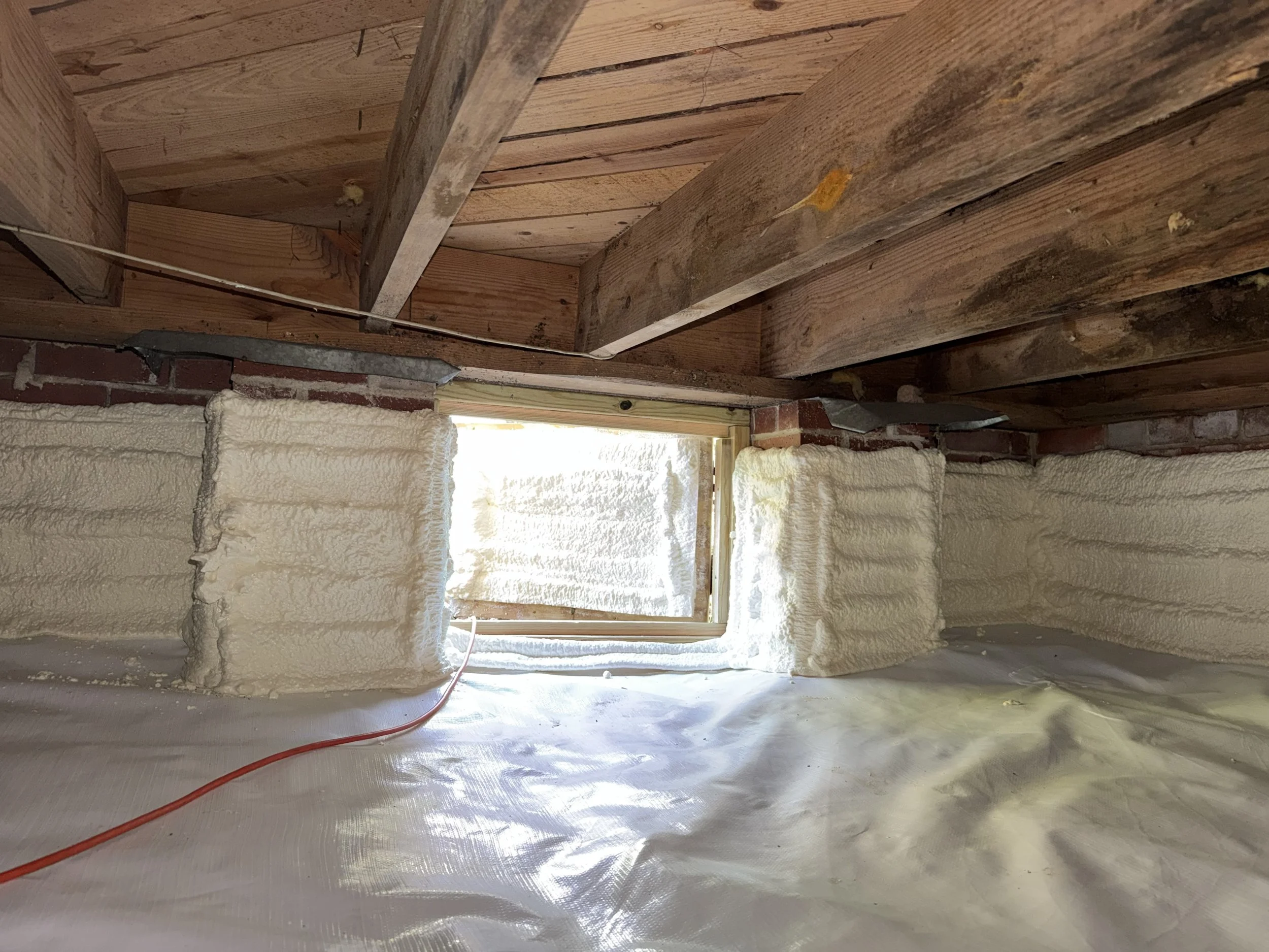 Cleaned crawl space floor joists after mold remediation, with evidence of prior moisture damage still visible above spray-foam foundation walls and a reinforced encapsulation liner.