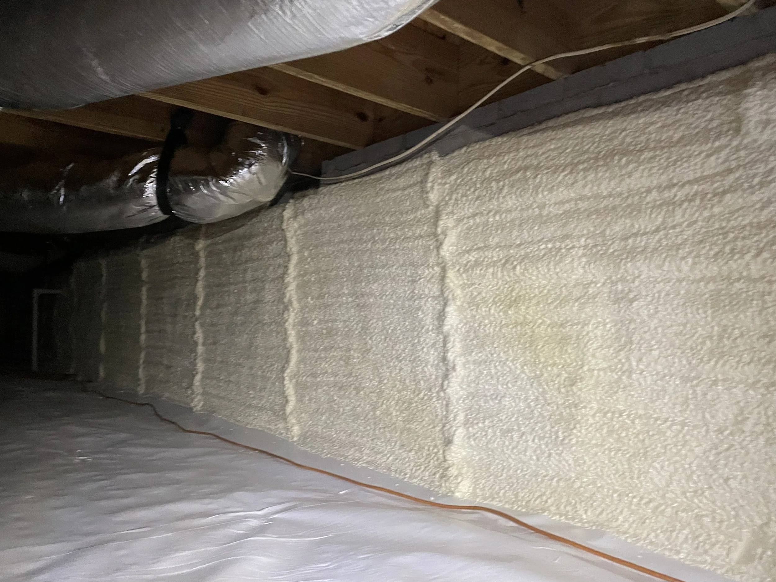 Spray foam insulation installed on a crawl space foundation wall above a sealed floor liner
