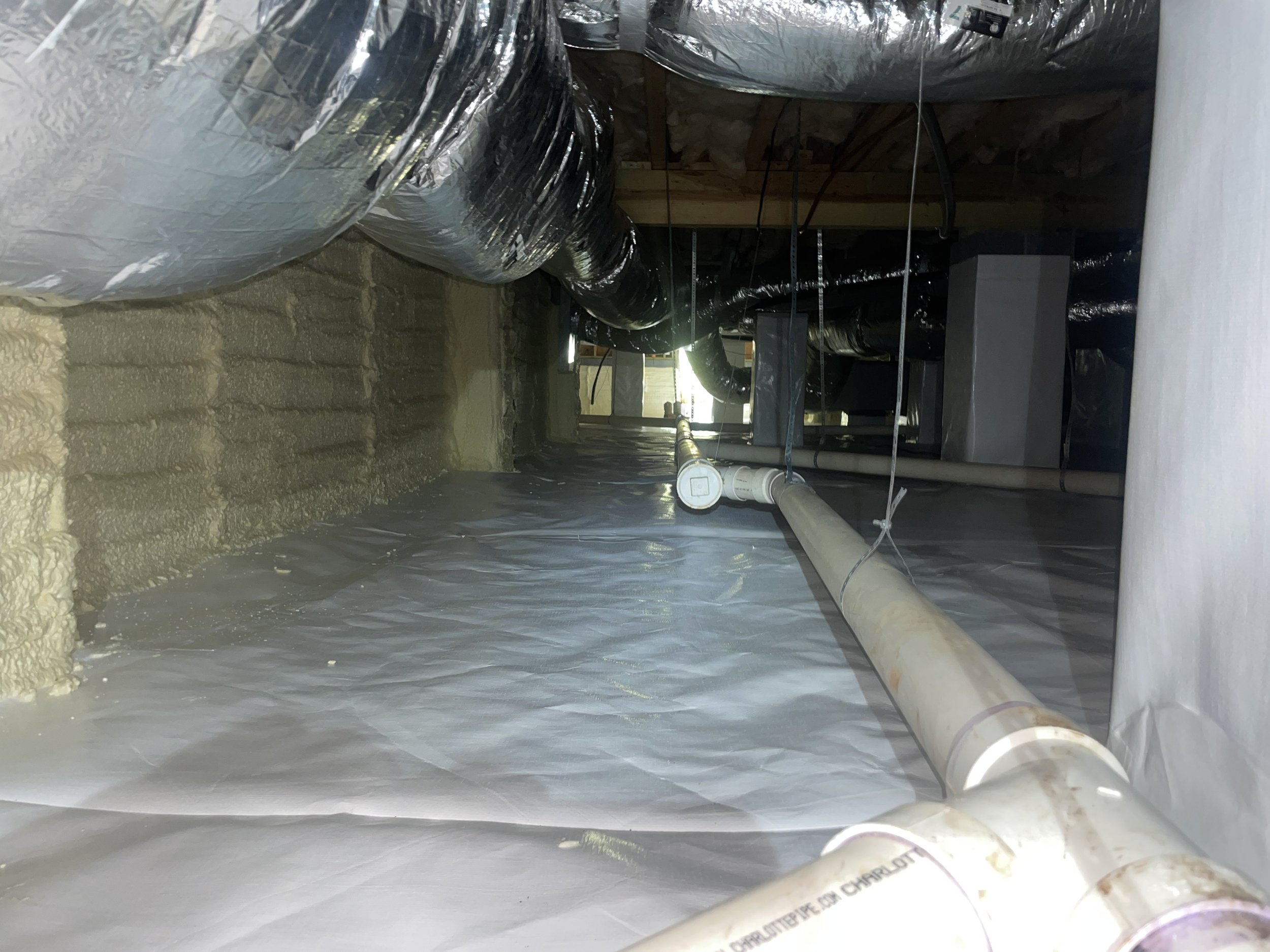 Encapsulated crawl space with sealed vapor barrier, dehumidifier, and spray foam insulation on the foundation walls to help control ground moisture, humid air and temperature conditions beneath the home
