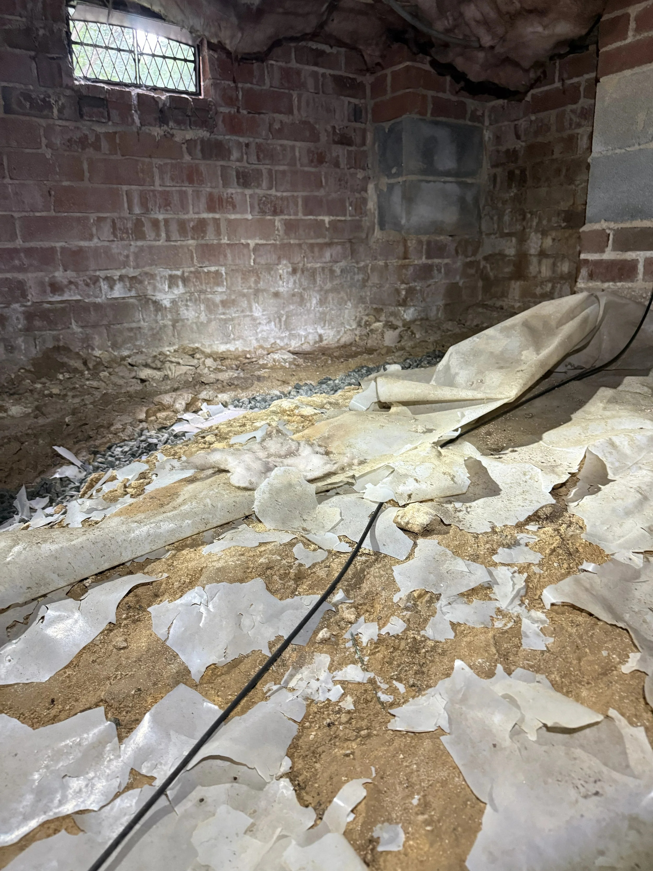 Damaged and deteriorated crawl space vapor barrier with torn plastic, exposed soil and debris leaving the ground moisture protection incomplete beneath the home