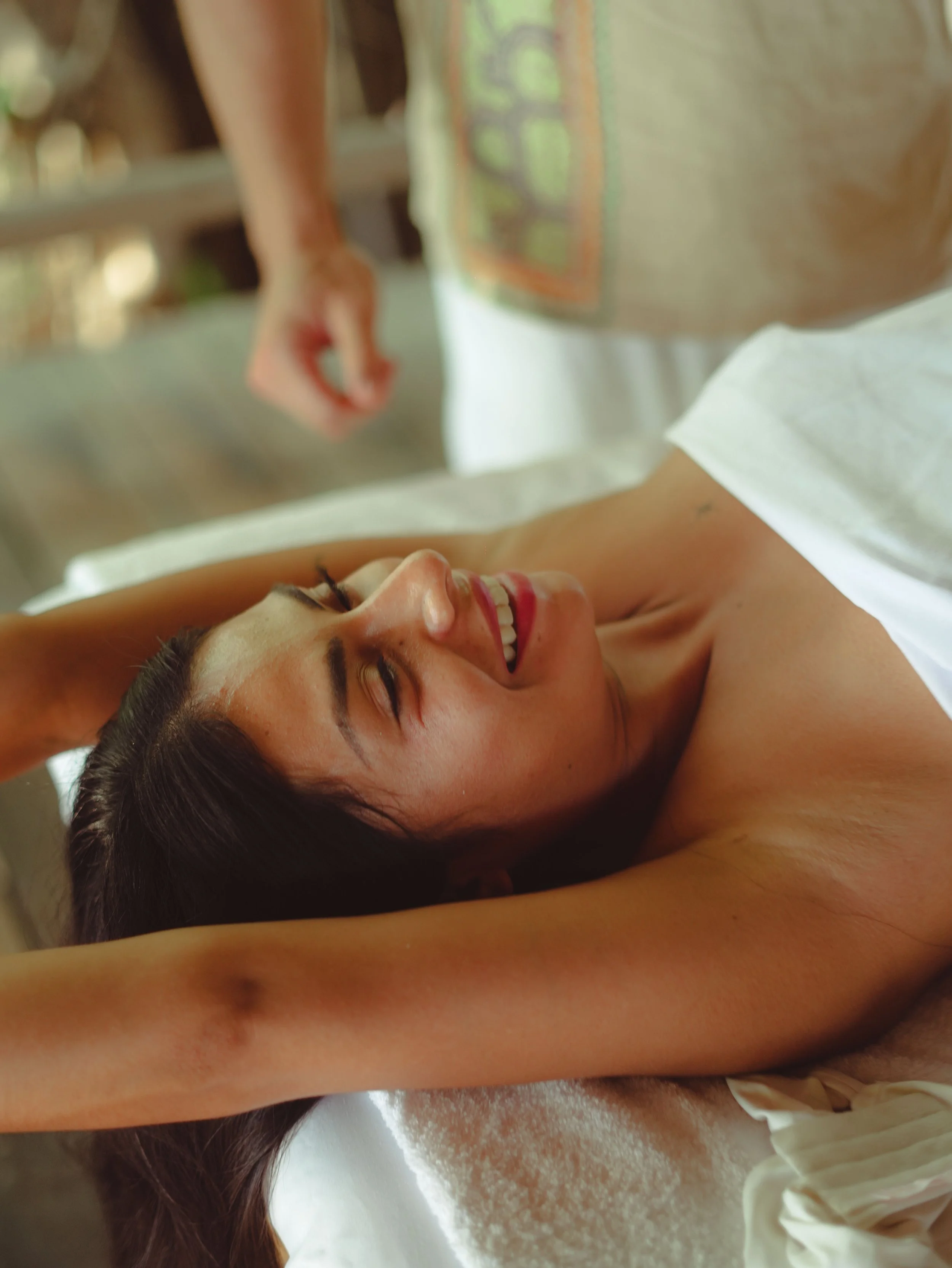 Zufriedene Kundin einer Massage, die auf einem Massagetisch liegend die Arme über den Kopf streckt. Ihr Gesicht bringt ihre positive Erfahrung bei Shipibo Massage Osnabrück zum Ausdruck.