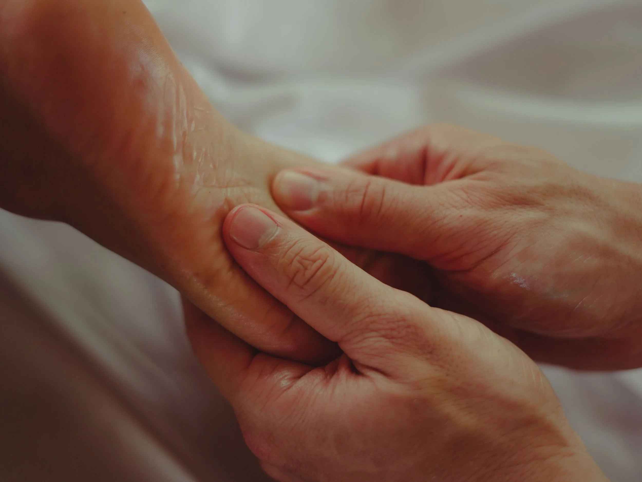 Nahaufnahme einer Fußmassage mit Massageöl. Die Fußfläche zeigt nach oben, zwei Hände umgreifen den Fußrücken und können so mit beiden Daumen die Fußsohle mit ihren Fußreflexzonen entspannen.
