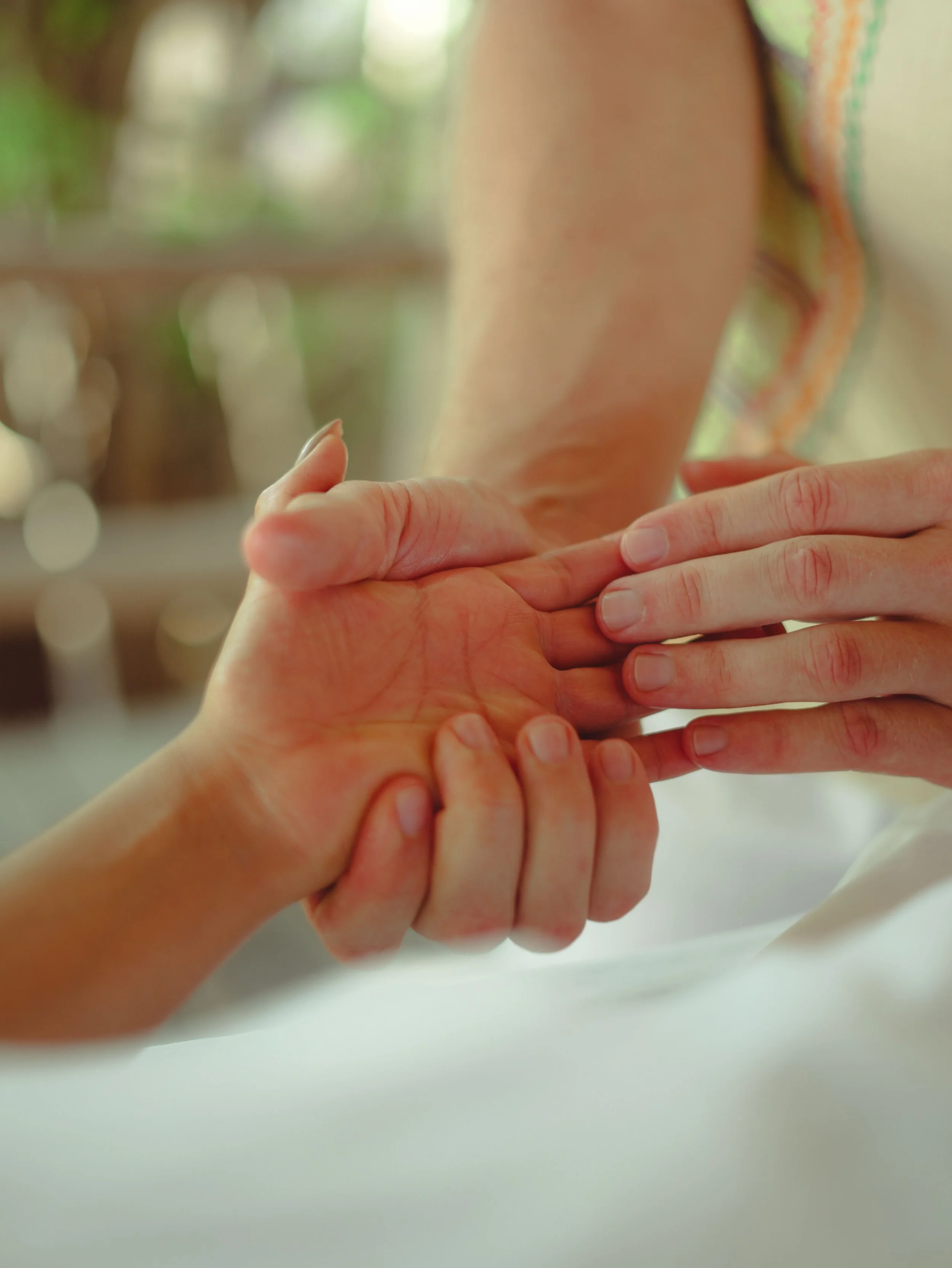 Nahaufnahme einer Handmassage. Die Handflächen der Kundin zeigen nach oben, während eine Hand des Masseurs diese von außen umgreift und mit der anderen mit den Fingern eine Fingermassage durchführt.