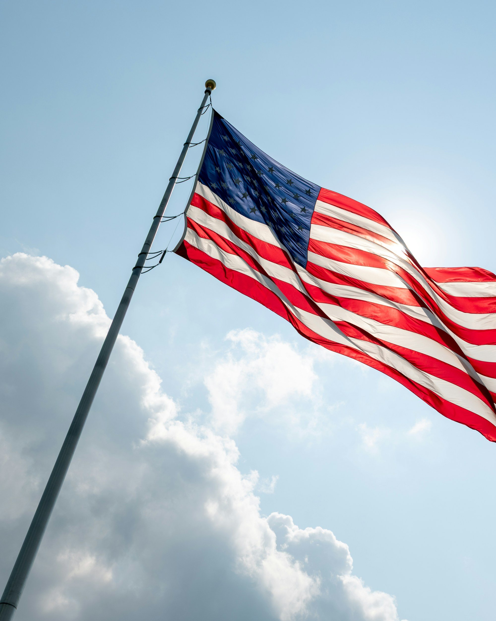 An American flag waving on a flagpole against a partly cloudy sky.