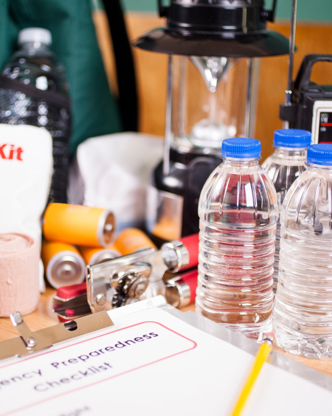 Emergency preparedness checklist on clipboard on a table with water bottles, batteries, a flashlight, and other supplies.