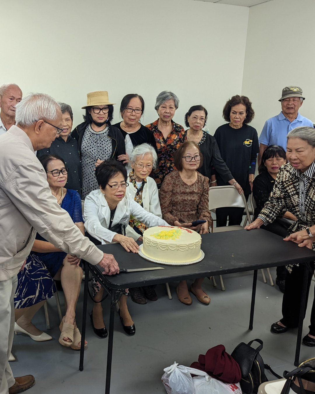 Group of elderly people gathered around a cake at a celebration event.