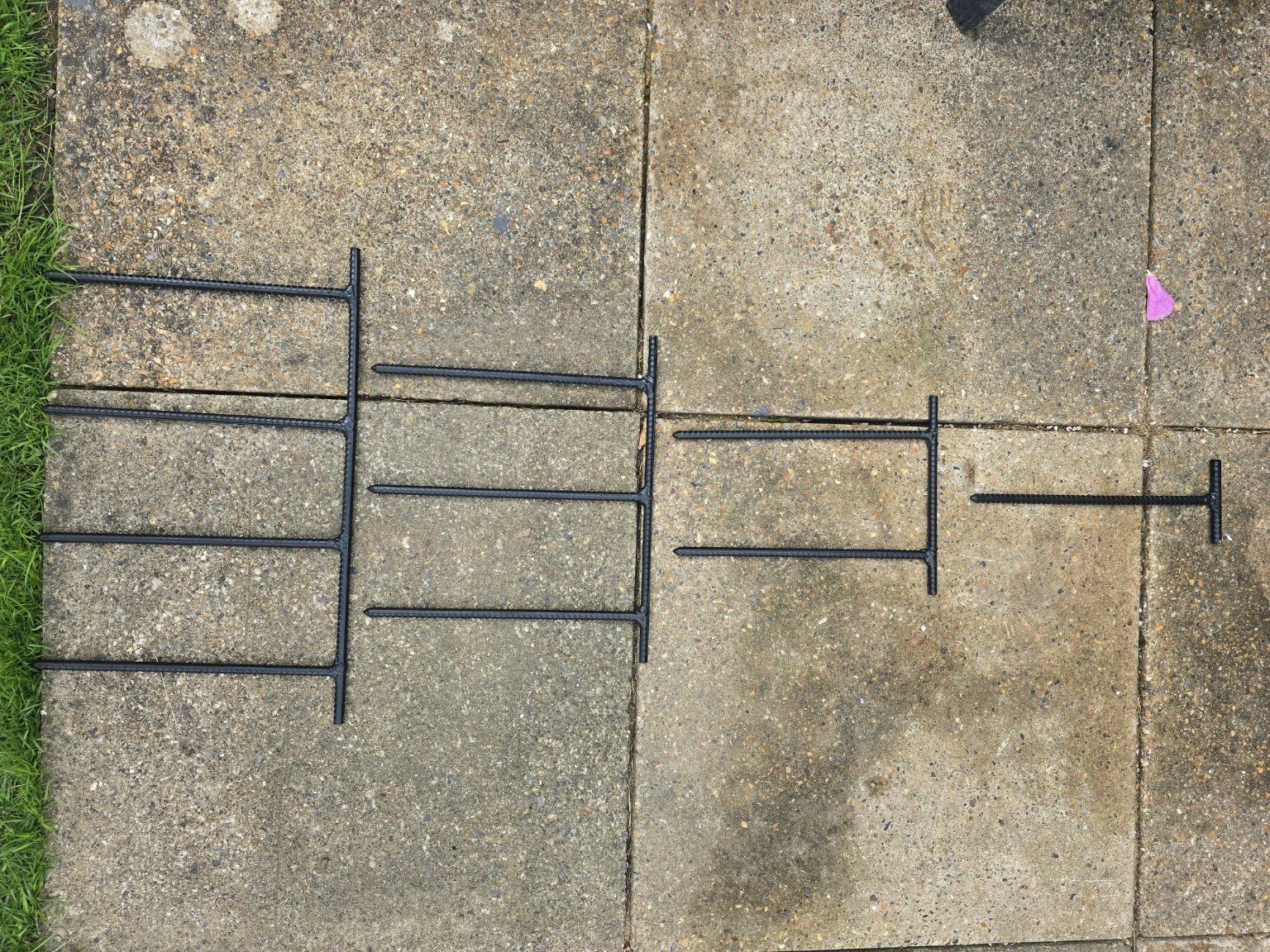 Disassembled black metal T-shaped rake or fork lying on concrete sidewalk with some pink paper or petal on the right side.