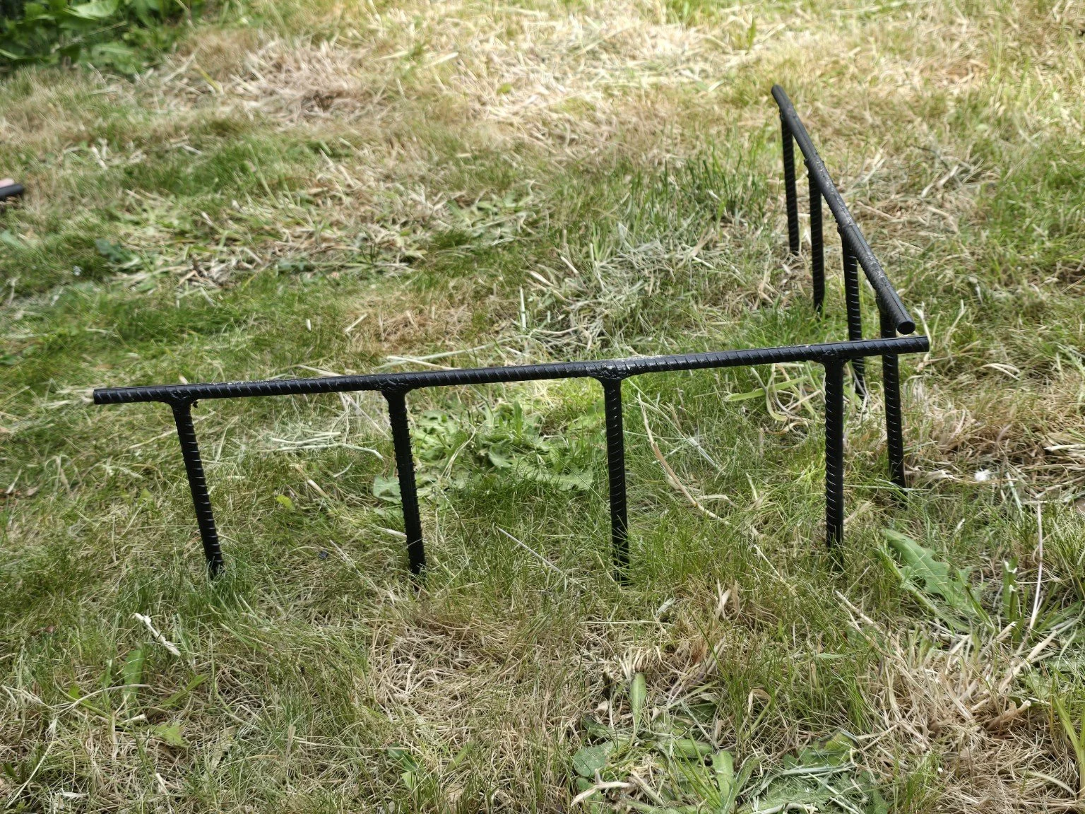 A rectangular black metal garden border on grass and dry vegetation.