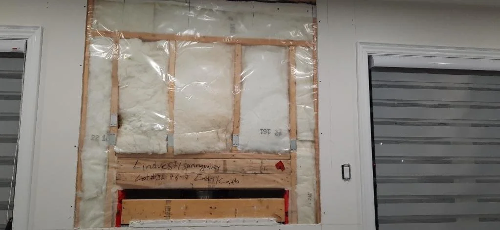 Interior wall insulation and wooden framework in a room in between two windows with closed white blinds.