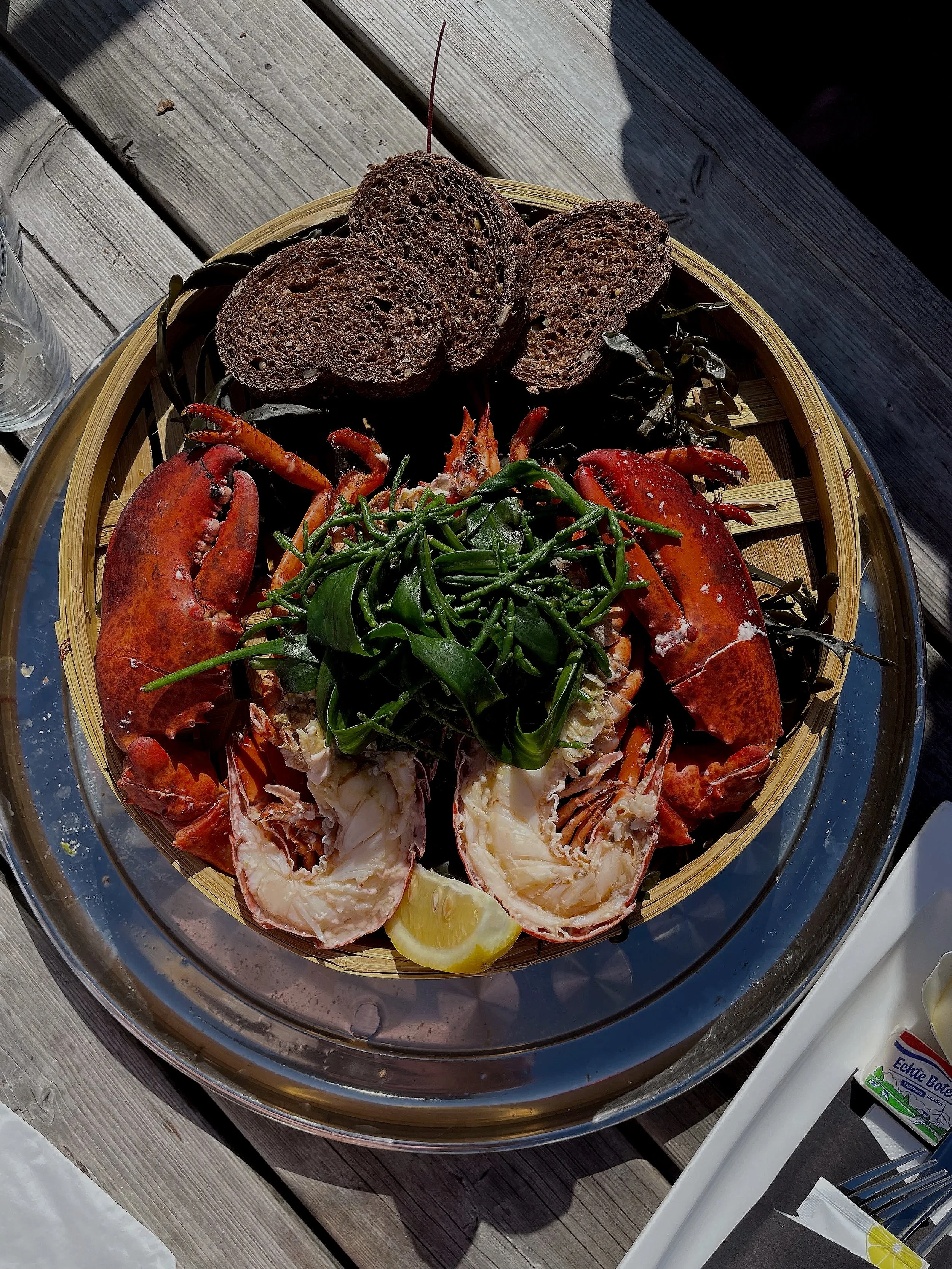 A seafood platter featuring lobster, crab, green herbs, lemon wedge, and slices of toasted bread on a decorative tray.