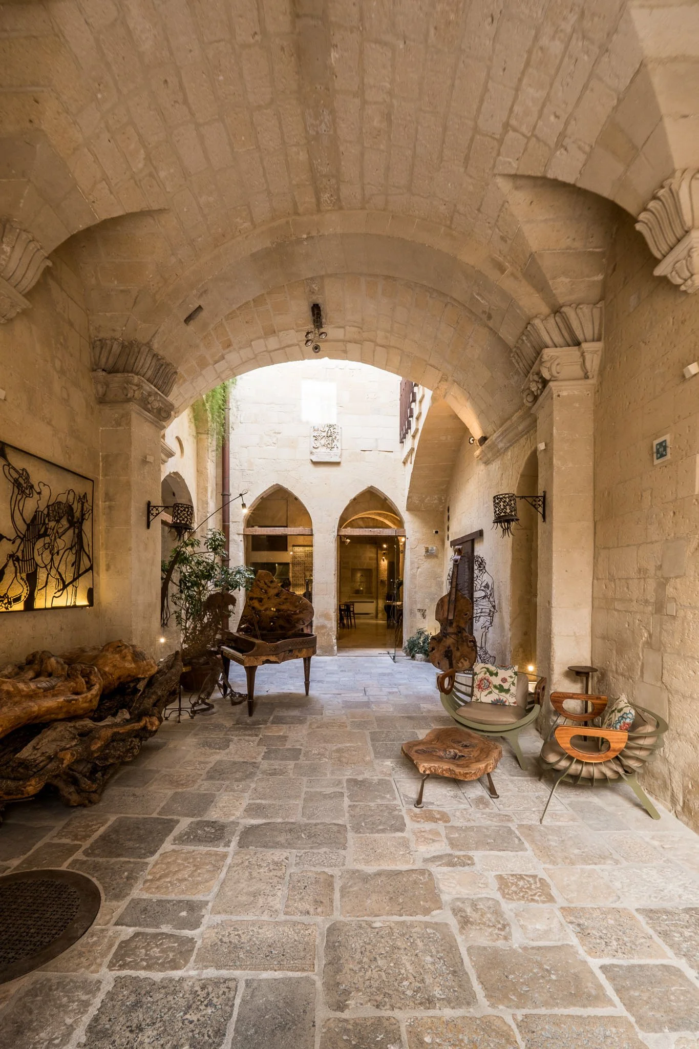 Interior view of a historic stone building with a vaulted ceiling, artistic furniture, and decorative elements, including sculptures and wall art, creating an elegant ambiance.
