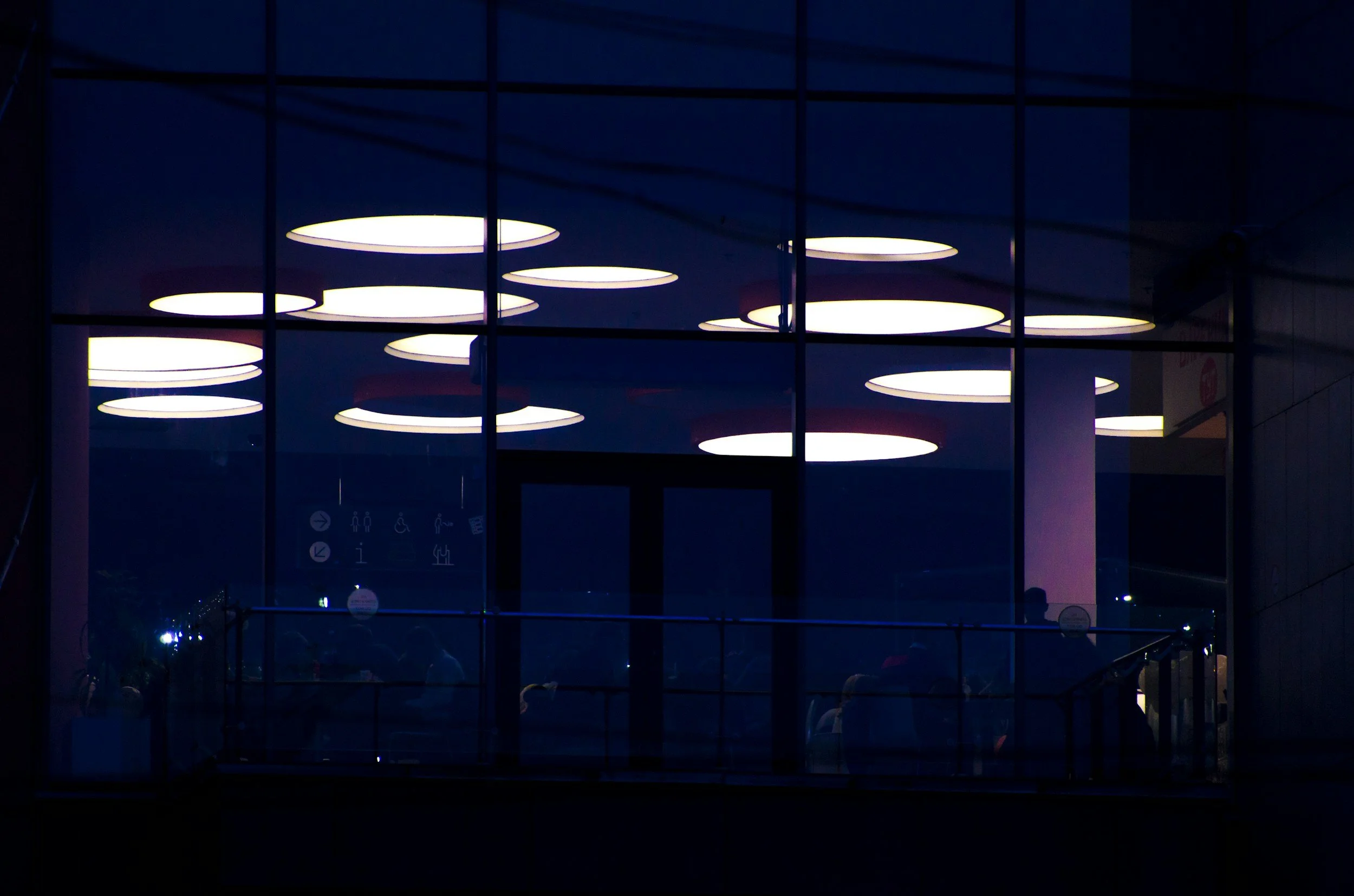 Nighttime view of illuminated circular ceiling lights through glass windows of a modern building.