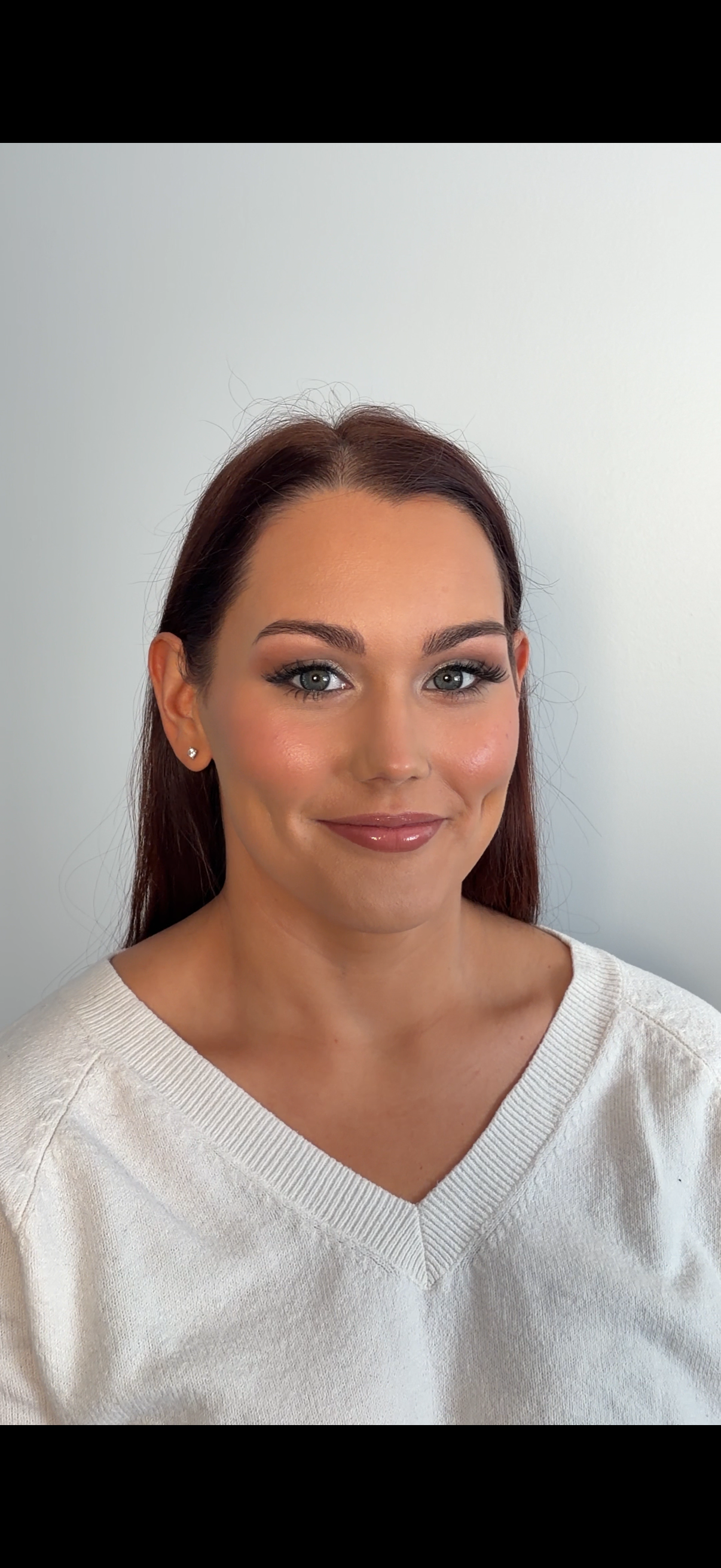 Portrait of a woman with long auburn hair, blue eyes, wearing a white sweater, smiling softly, against a plain light-colored background.