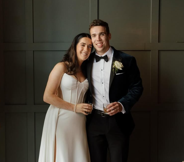 A happy couple dressed in wedding attire, standing together with drinks in hand, smiling at the camera.