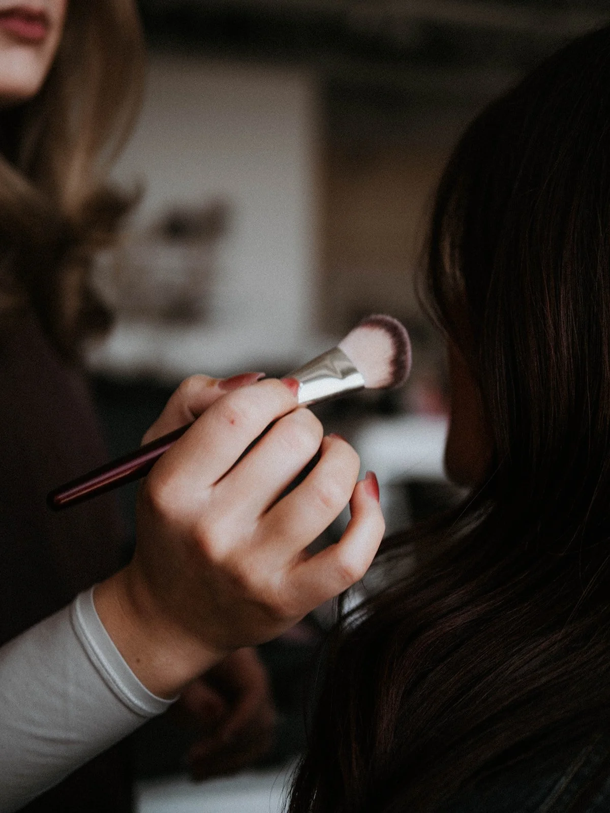 A makeup artist applying blush to a woman's cheek with a makeup brush.
