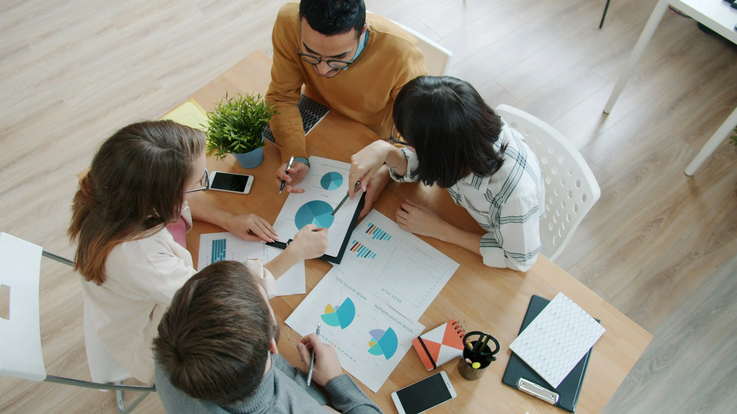 Eine Gruppe von Menschen arbeitet an einem Tisch mit Diagrammen und Berichten, während sie eine Präsentation besprechen.